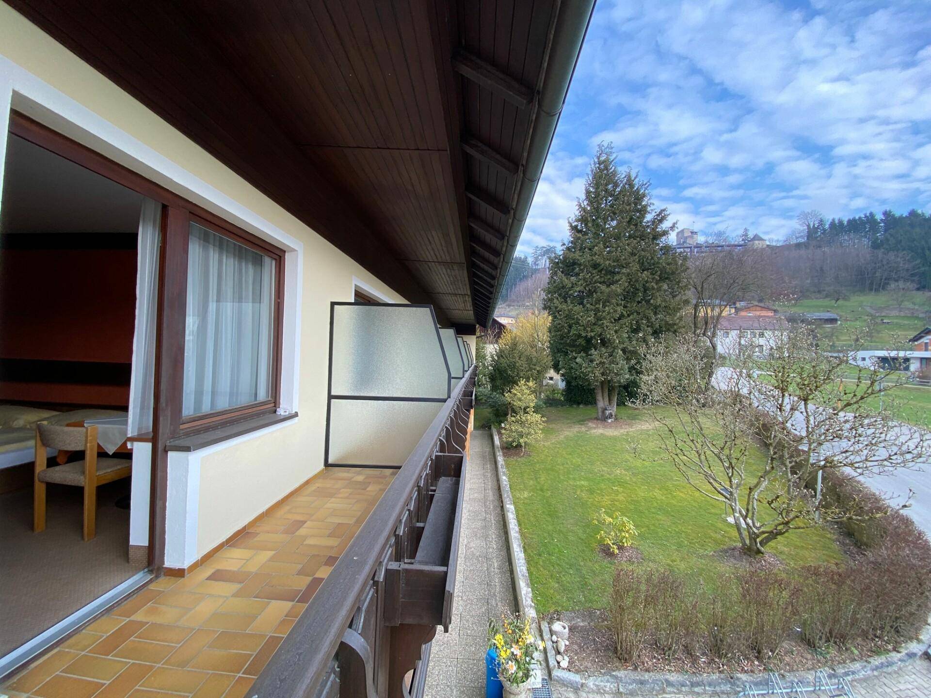 Langer Balkon mit Fliesenboden und Blick auf die grüne Landschaft und umliegende Häuser.