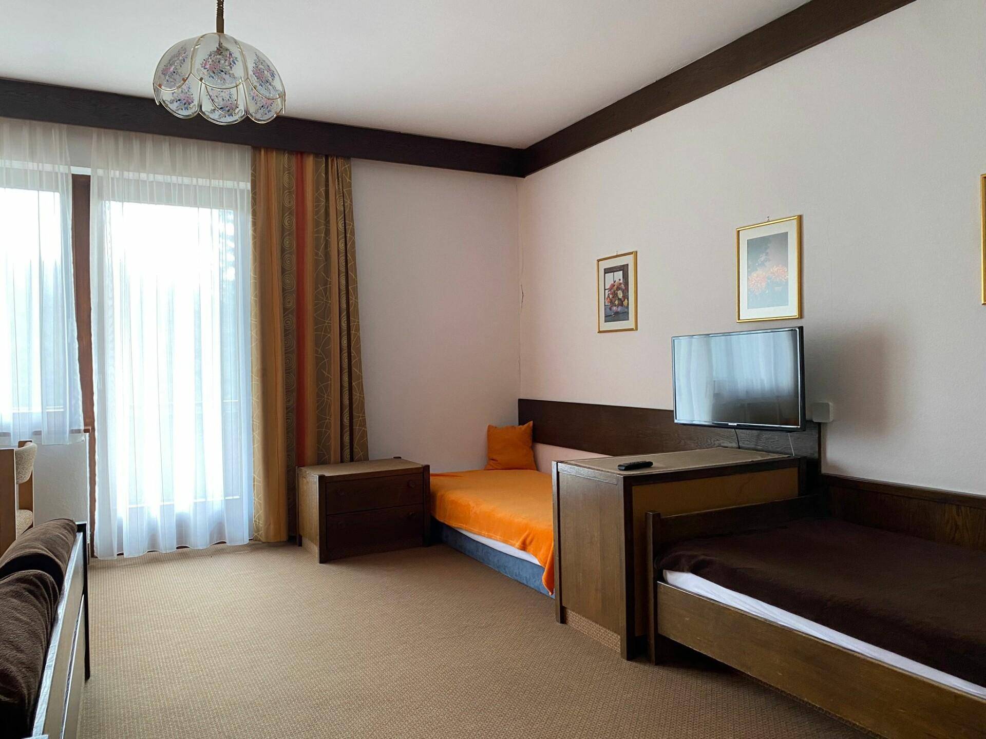 Helles Schlafzimmer mit Einzelbetten, Teppichboden und einem Fernseher an der Wand.