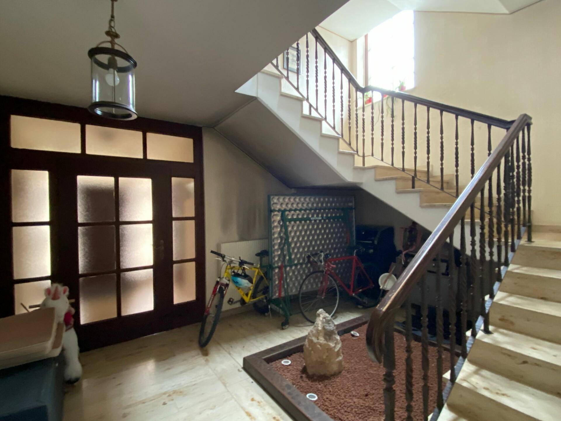 Treppenhaus mit Holzgeländer, Marmorboden und einem kleinen Zen-Garten unter der Treppe.