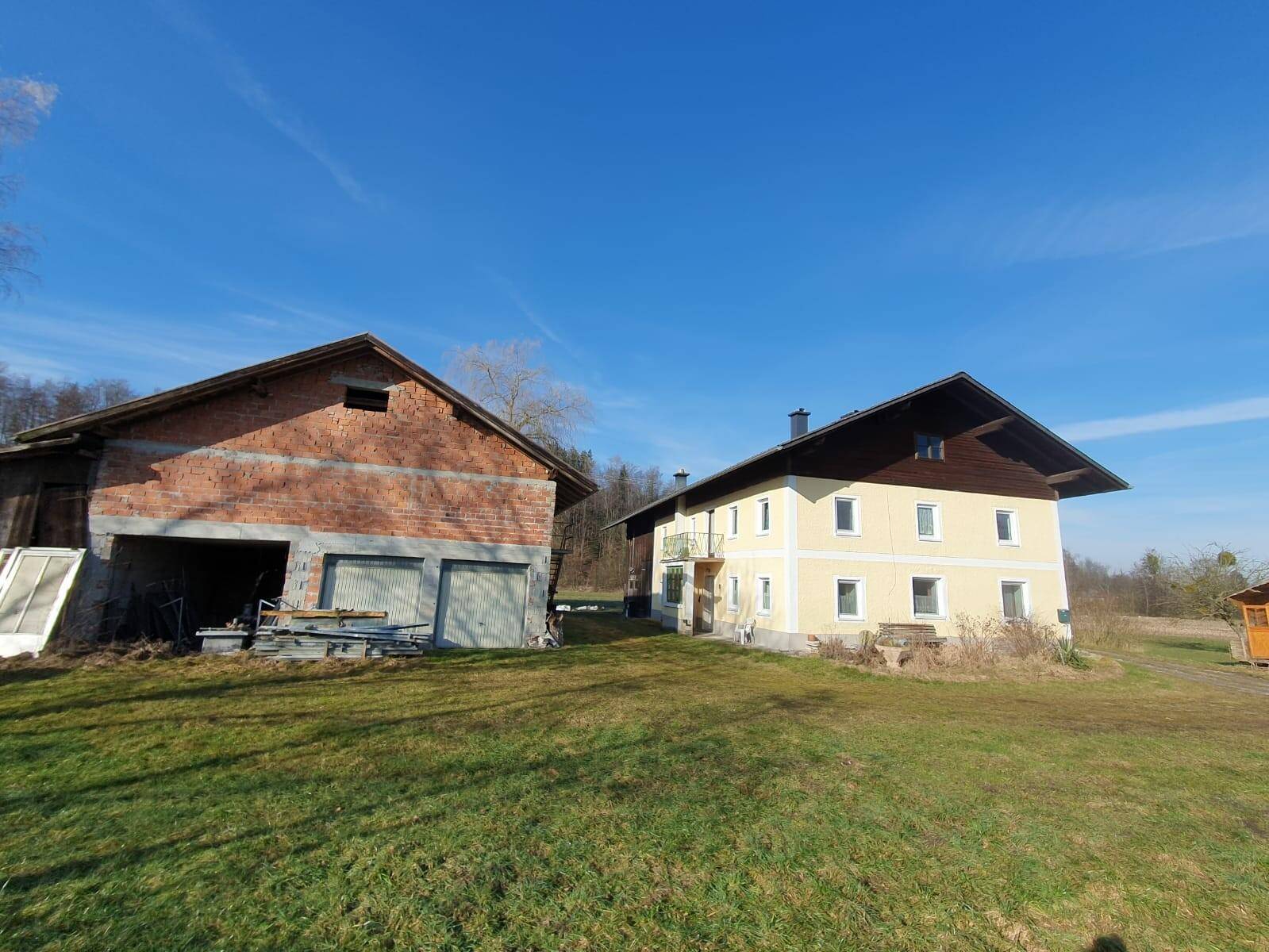 Zwei Gebäude auf einem großen Grundstück mit gelbem Wohnhaus und Scheune unter blauem Himmel.