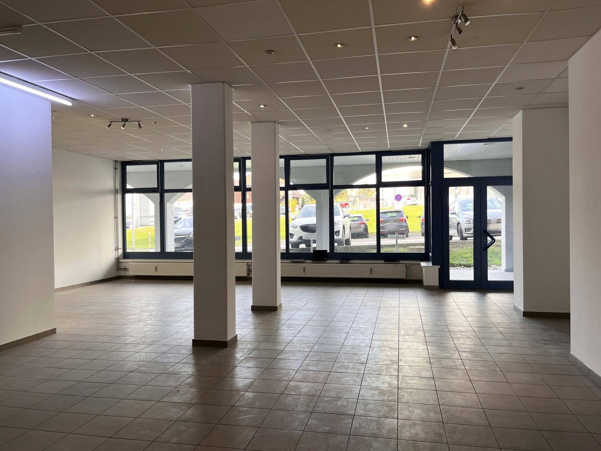Heller Gewerberaum mit großen Schaufenstern, Fliesenboden und Zugang zur Straße, geeignet für verschiedene Nutzungen.