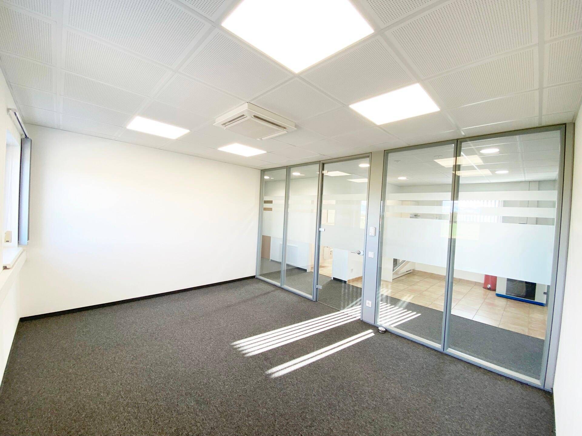 Modernes Büro mit Teppichboden und Glaswänden, die den Blick in angrenzende Räume freigeben.