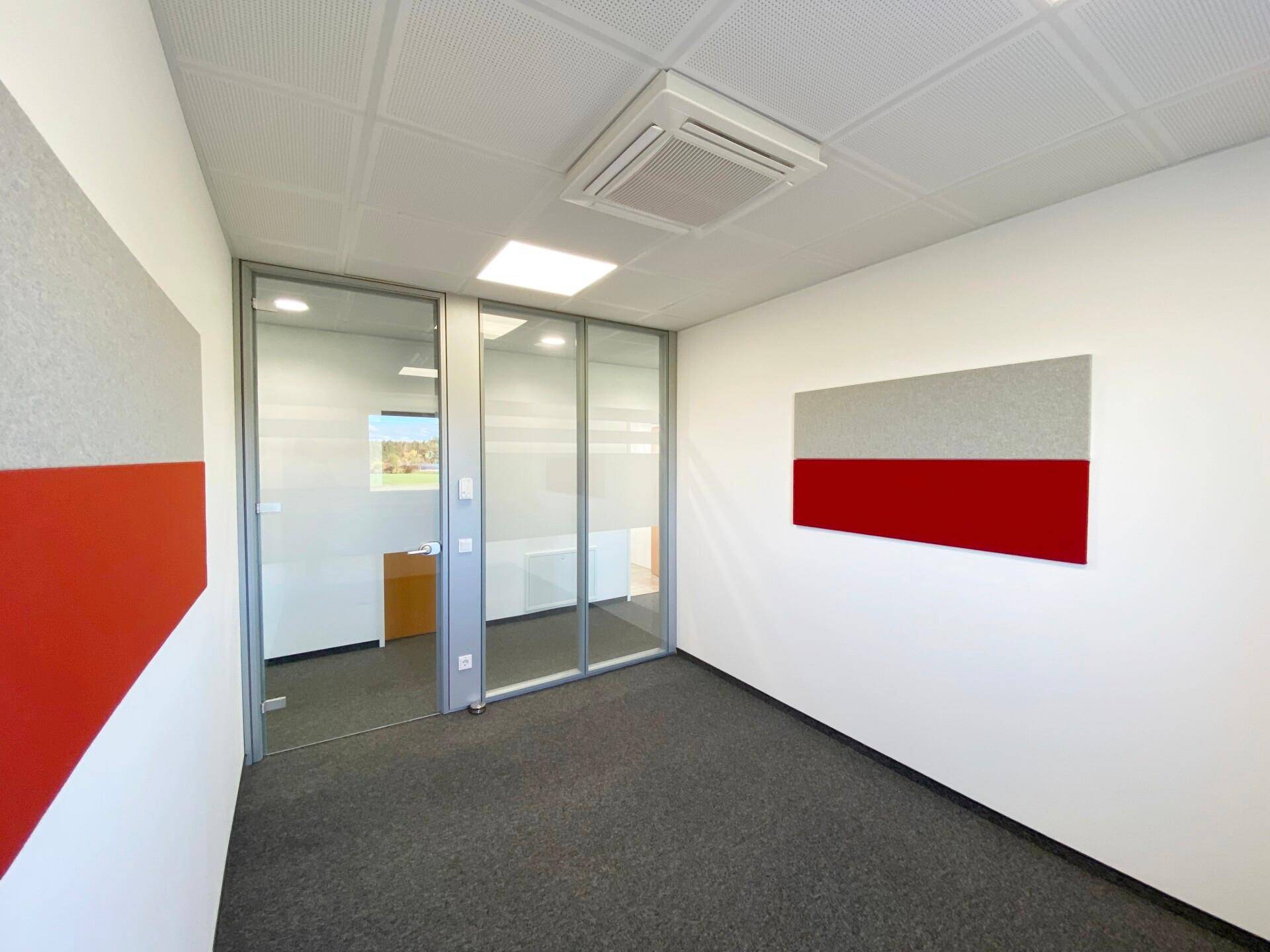 Büro mit Teppichboden, Glaswänden und dekorativen rot-grauen Akustikpaneelen an den Wänden.