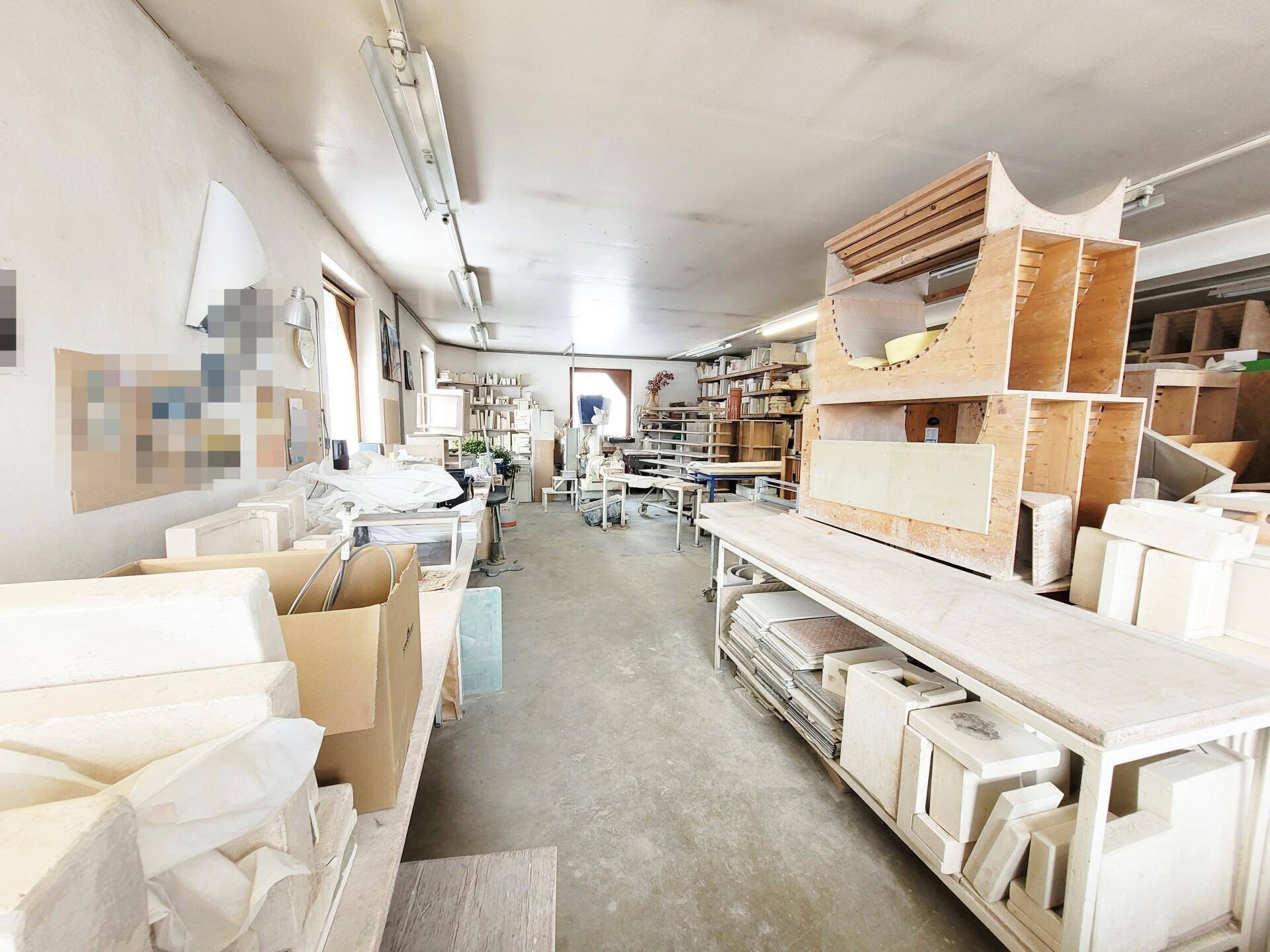 Heller Werkstattraum mit verschiedenen Arbeitsbereichen und Materialien auf Regalen.