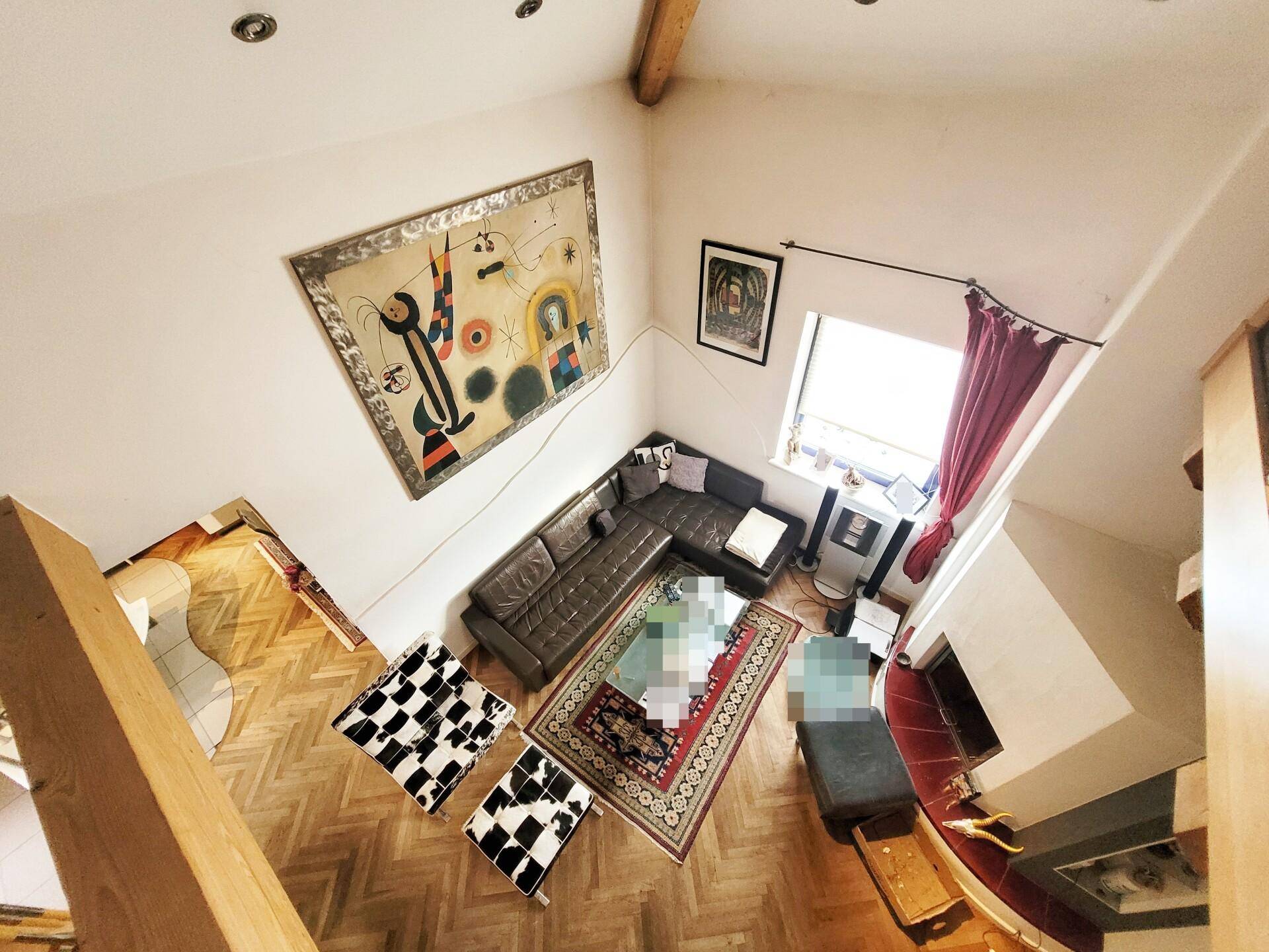 Blick von oben auf ein stilvolles Wohnzimmer mit Ledersofa, Teppichen und großem Fenster.