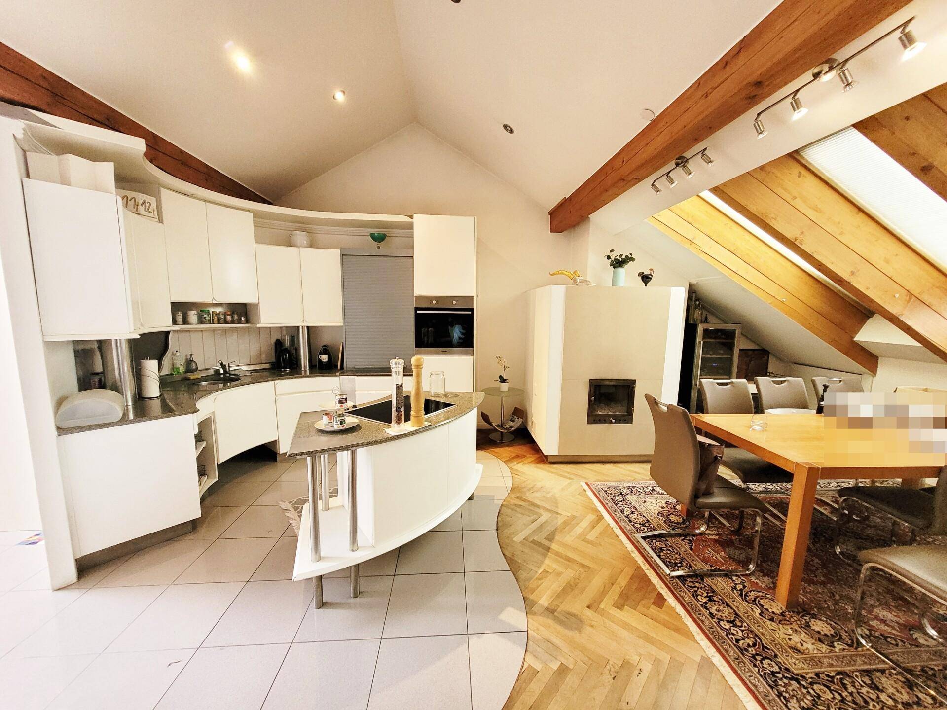 Moderne Küche mit weißen Schränken, Essbereich und Kamin unter einer Dachschräge.