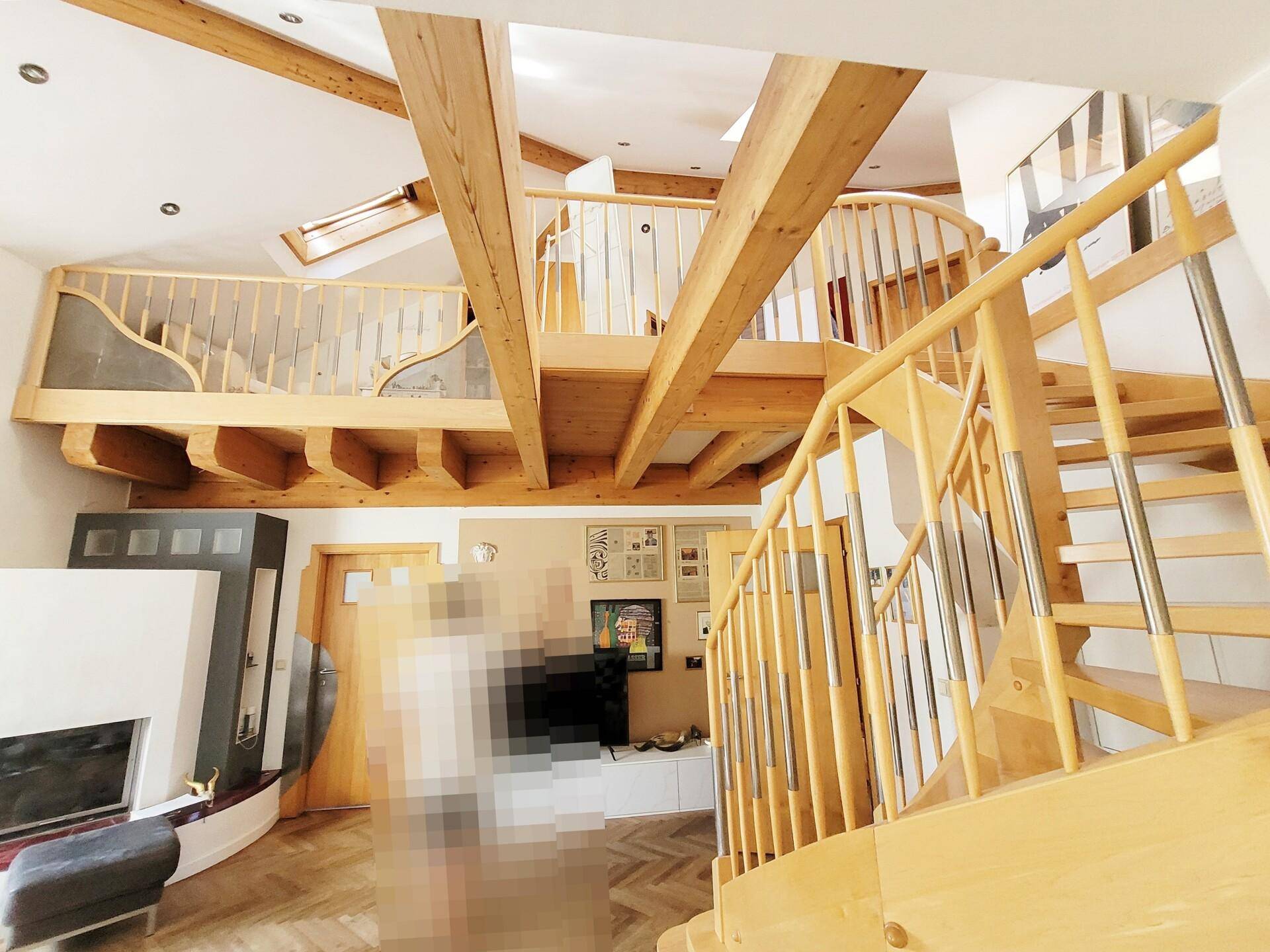 Helles Wohnzimmer mit hoher Decke, Holzbalken und einer offenen Galerie mit Holztreppe.
