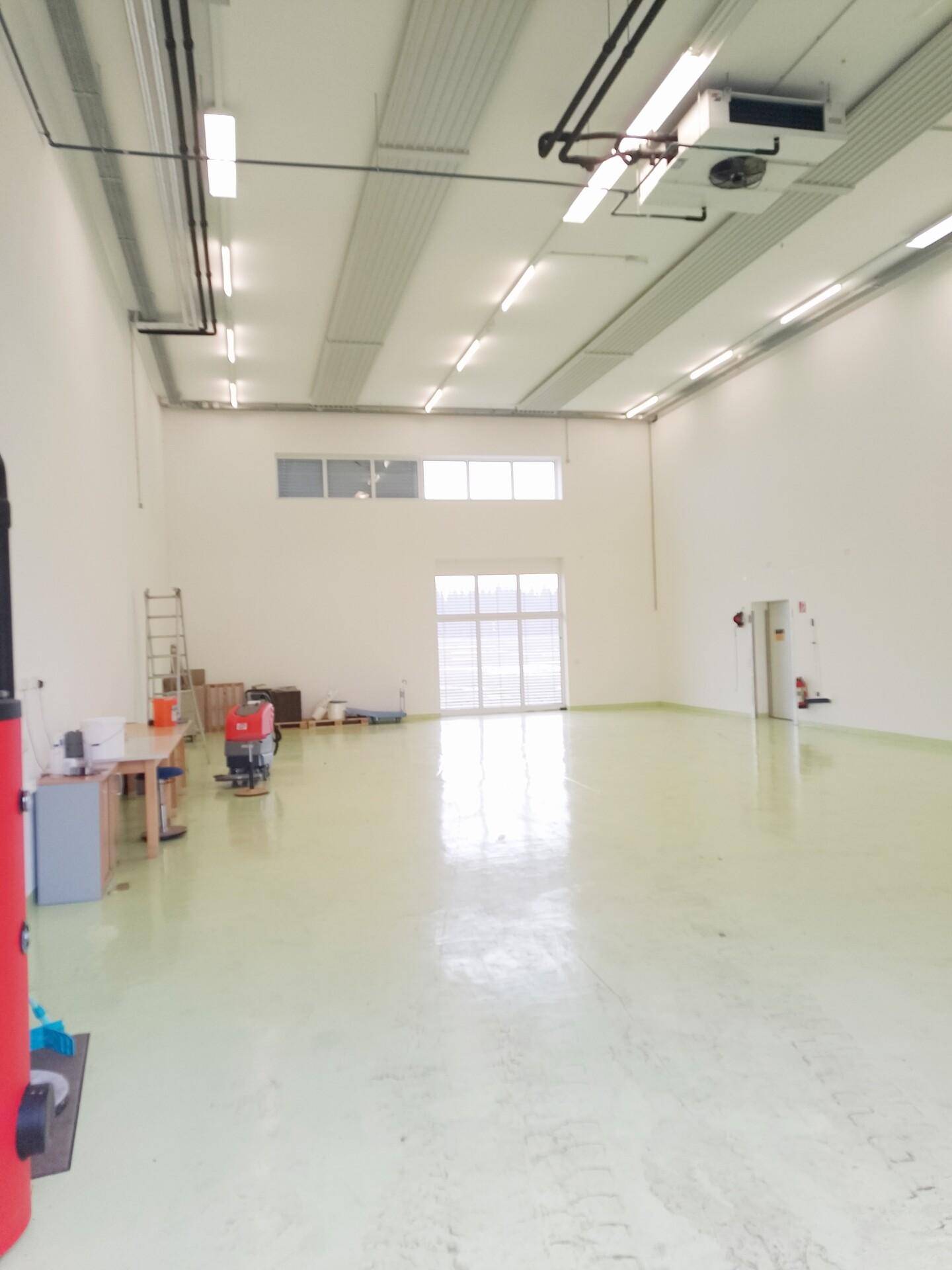 Geräumige Lagerhalle mit hohen Decken, glänzendem Boden und großen Toren für den Zugang.