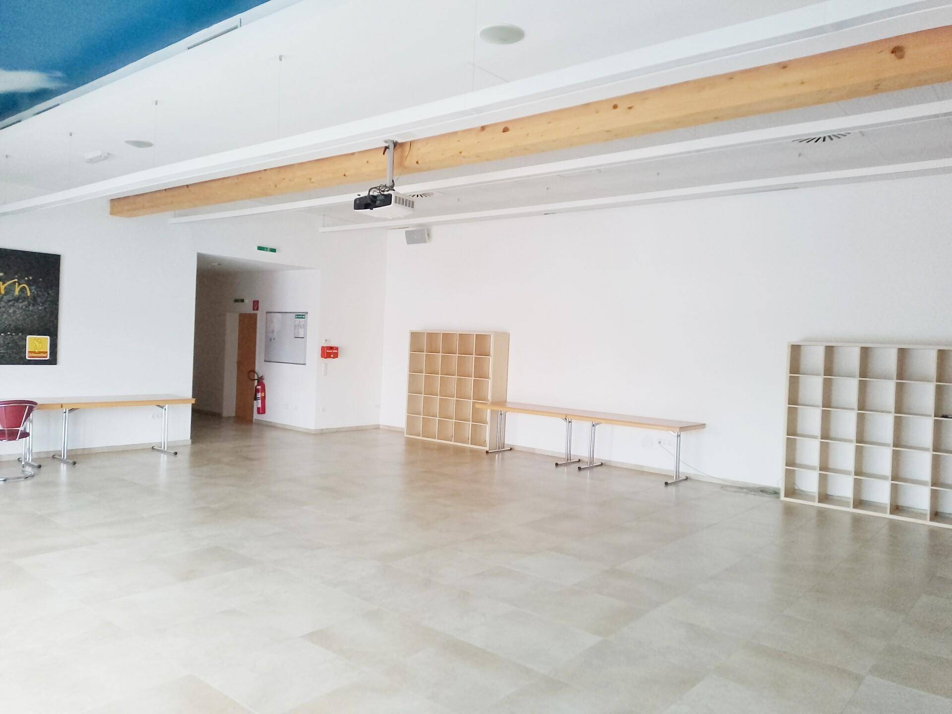 Großer Mehrzweckraum mit hellem Fliesenboden, Holzbalken und flexibler Möblierung.