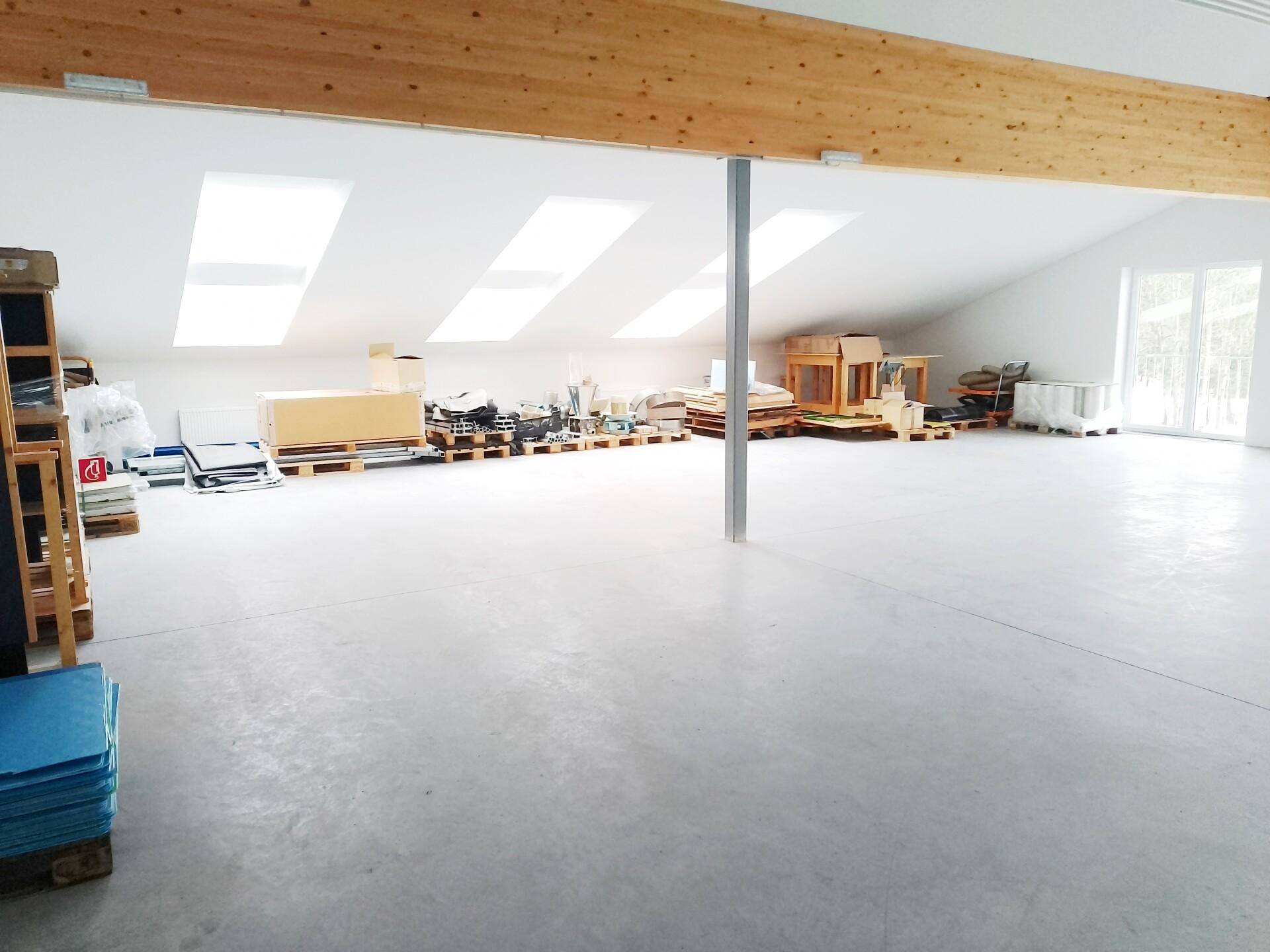 Geräumiger Lagerbereich im Dachgeschoss mit schrägen Decken, Dachfenstern und gelagerten Materialien.