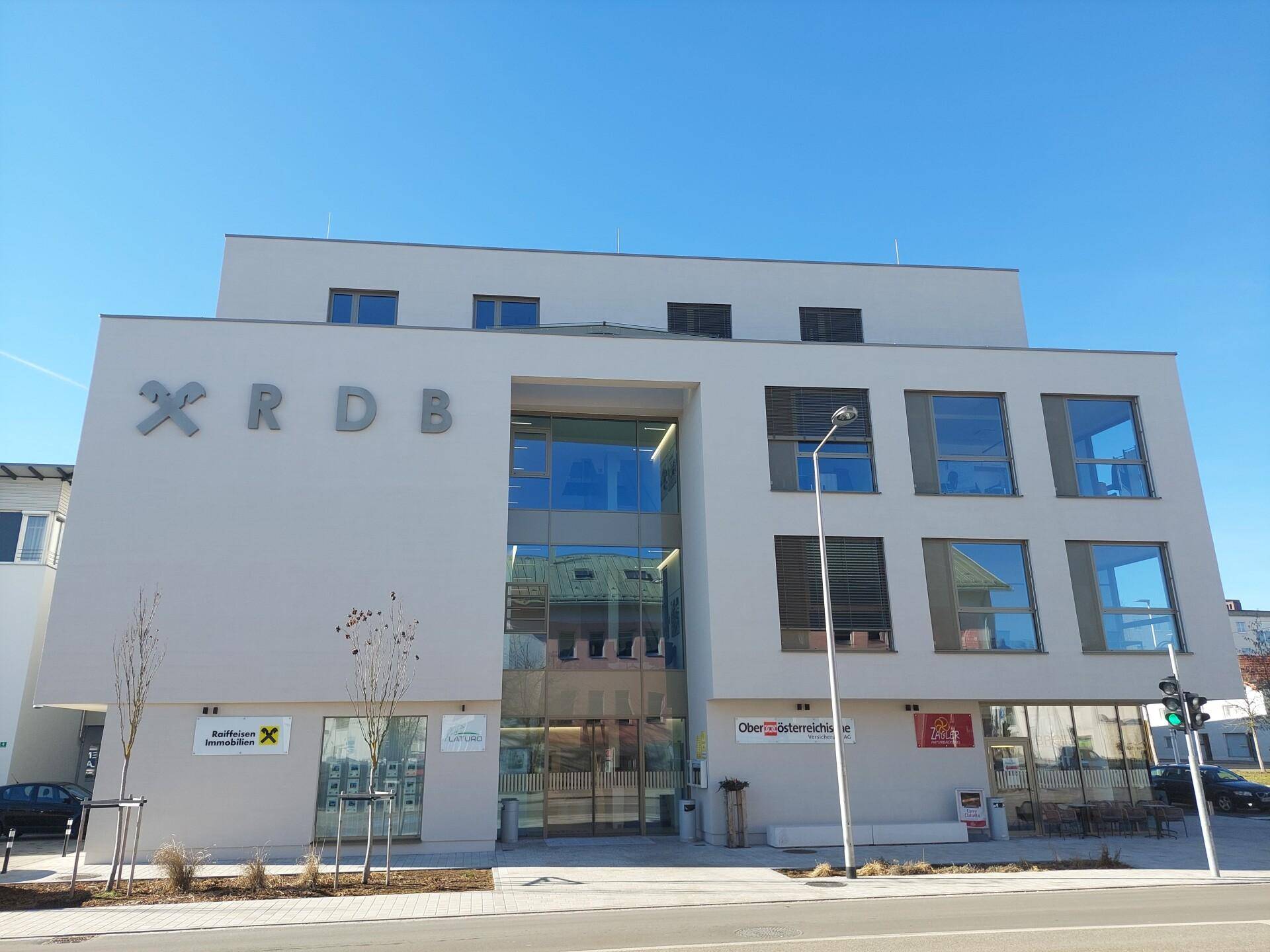 Modernes Geschäftsgebäude mit heller Fassade und großen Glasflächen unter blauem Himmel.