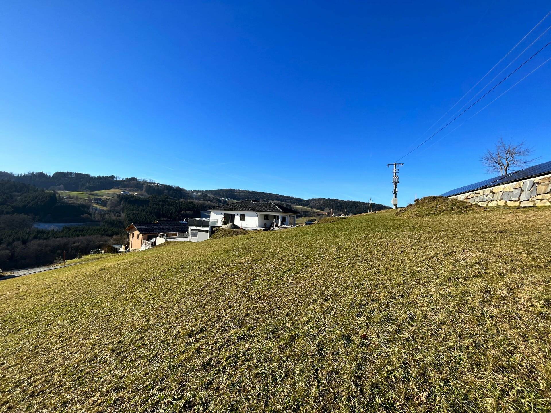 Weitläufige grüne Wiesen mit Blick auf ein Wohnhaus und die umliegende hügelige Landschaft.