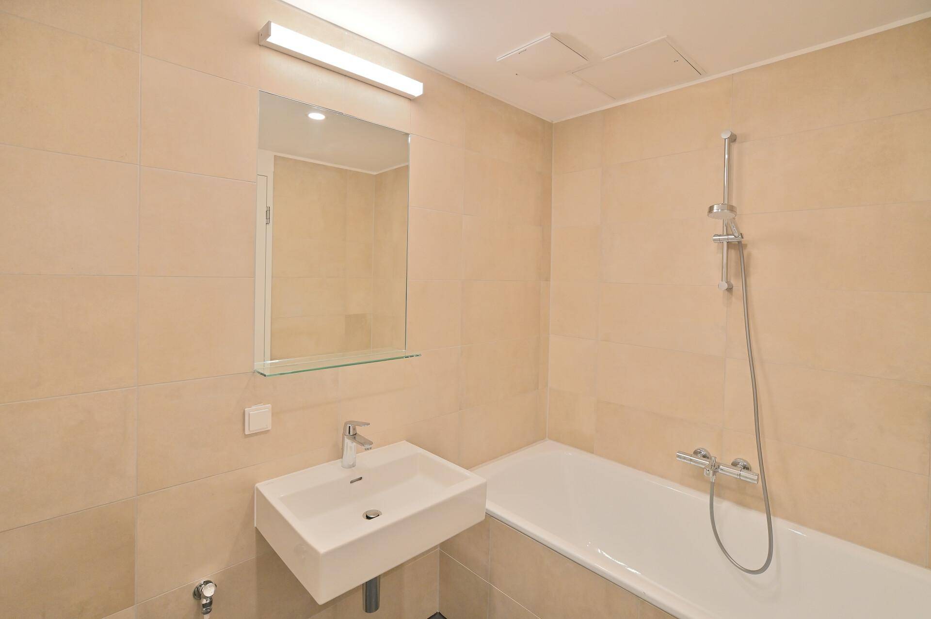 Funktionales Badezimmer mit beigefarbenen Fliesen, Badewanne und modernem Waschbecken.