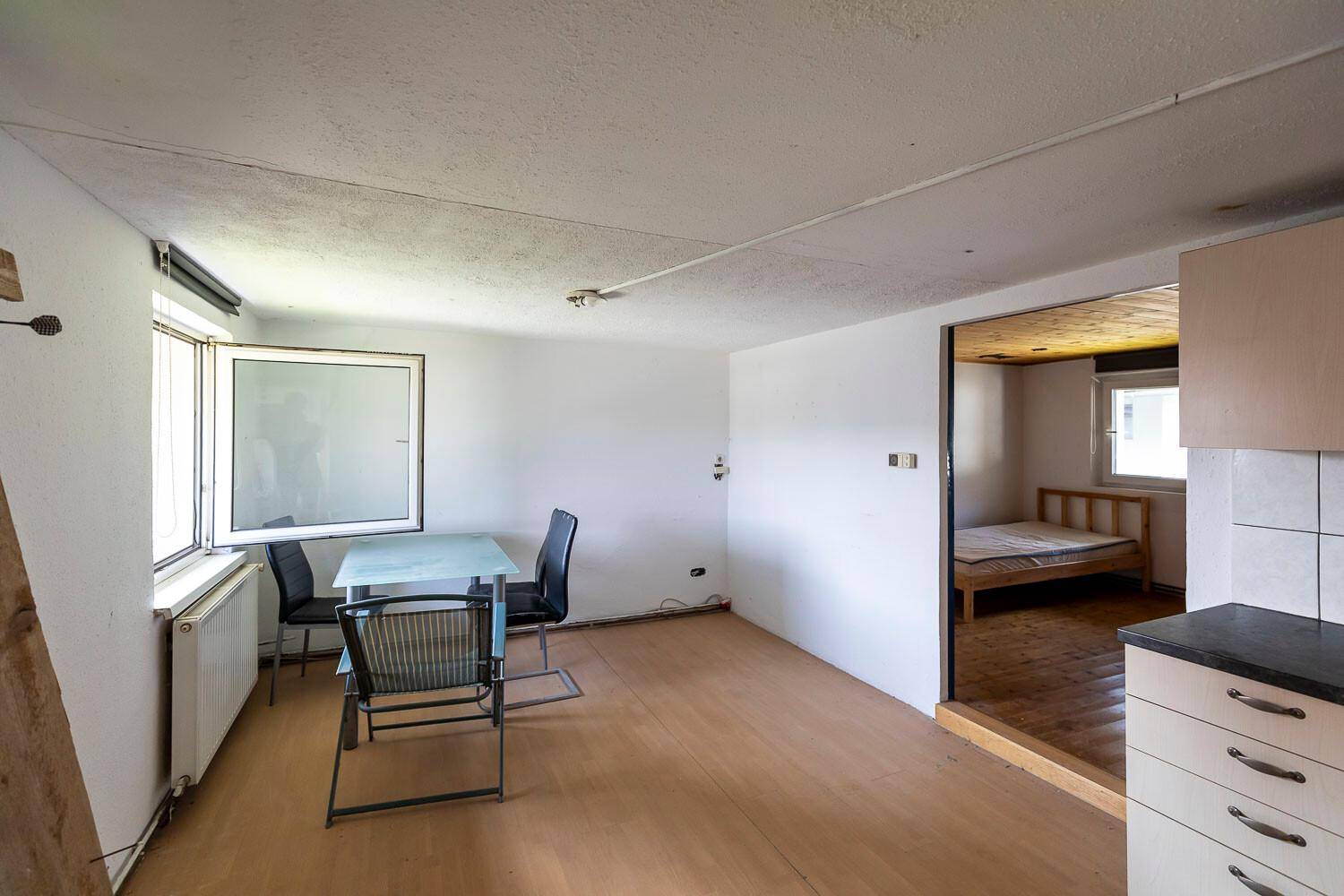 Heller Wohnbereich mit kleinem Esstisch, Laminatboden und Zugang zu einem Schlafzimmer.