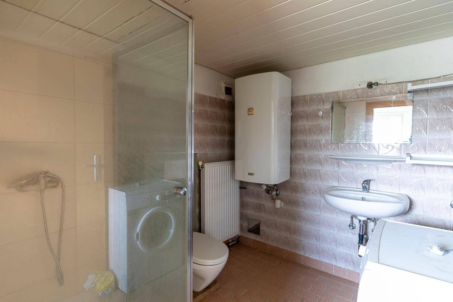Badezimmer mit Dusche, WC, Waschbecken und einer Waschmaschine in einfacher Ausstattung.