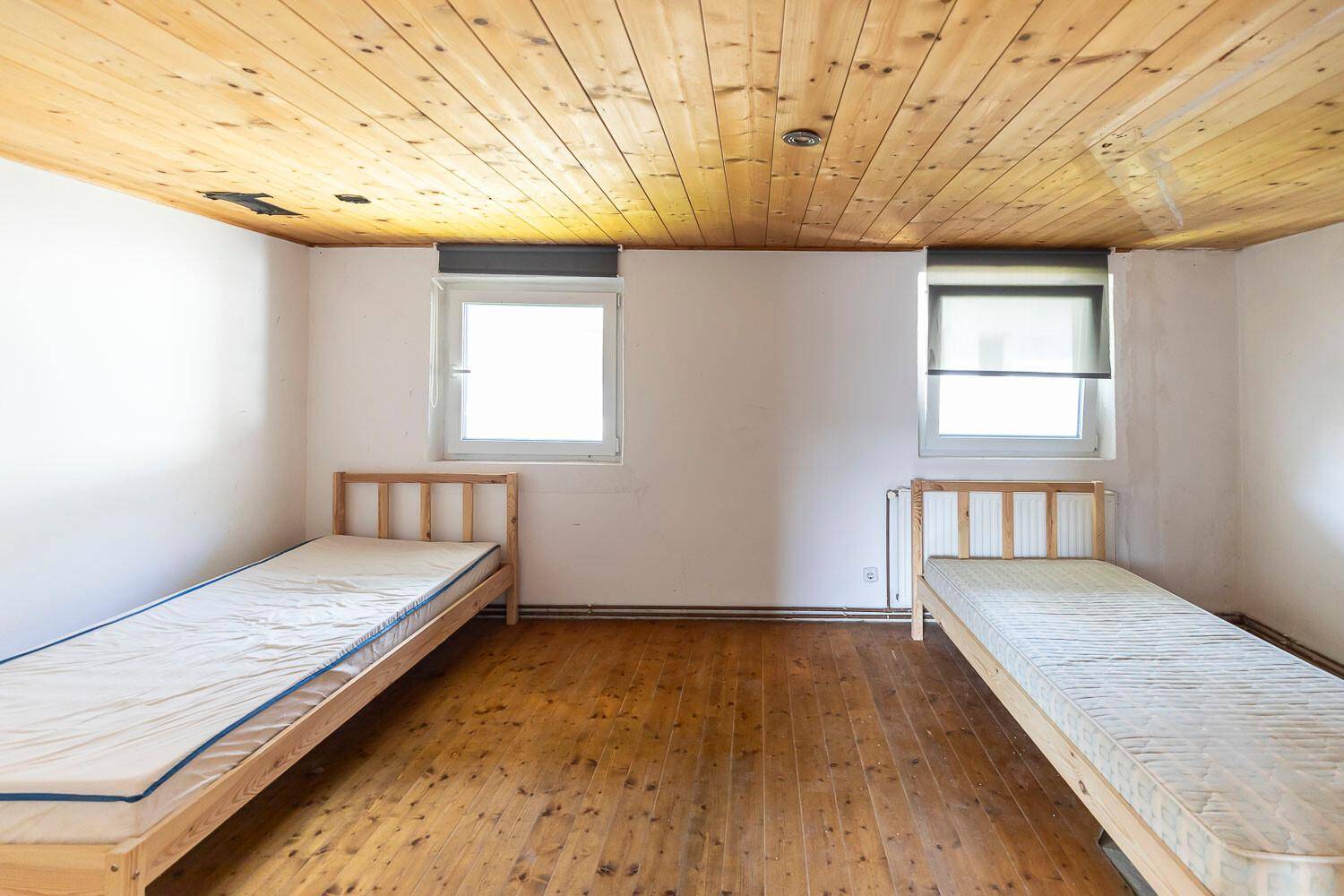 Schlafzimmer mit zwei Einzelbetten, Holzdielenboden und einer Holzdecke.