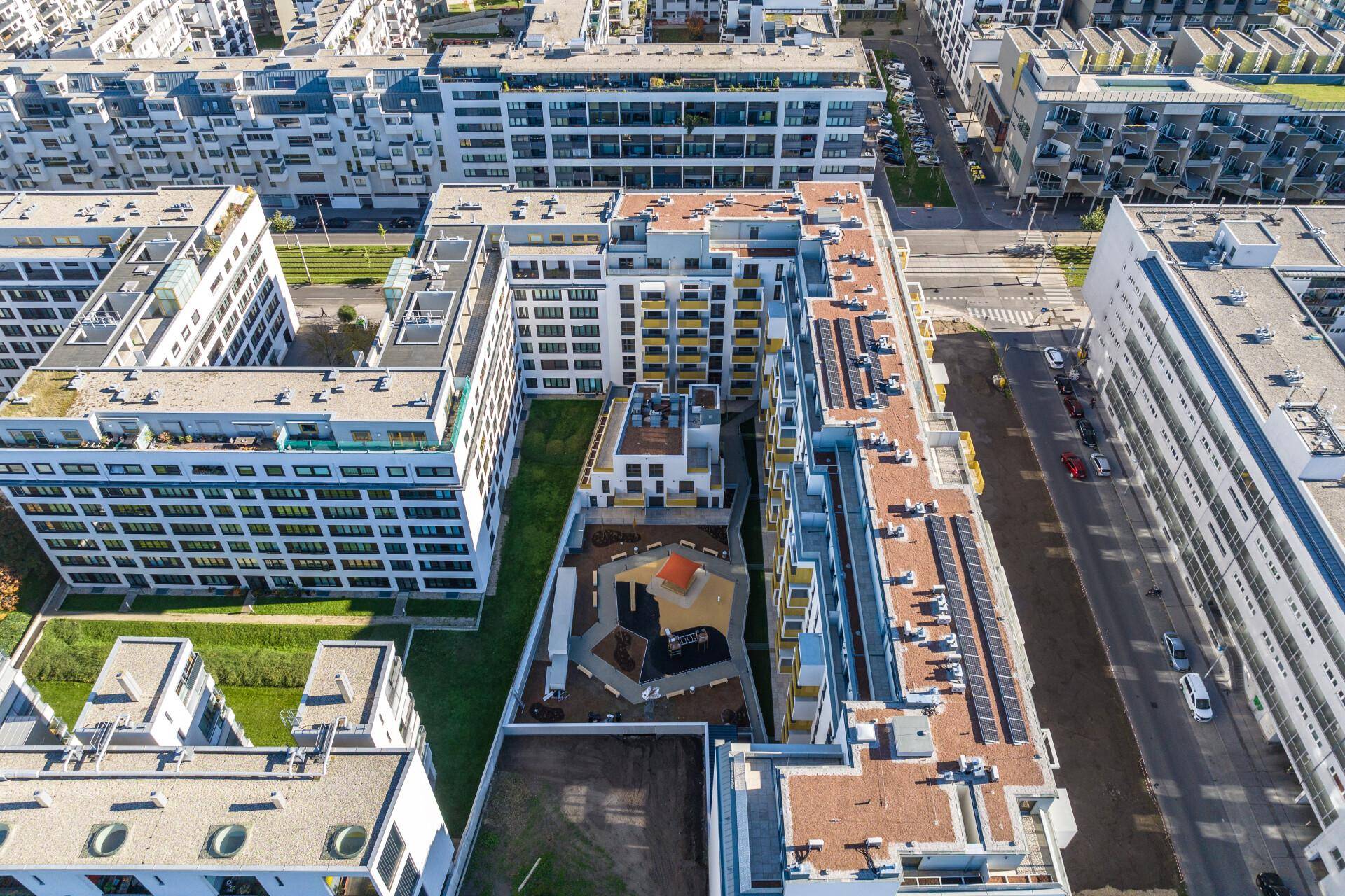 Luftaufnahme eines modernen Wohnkomplexes mit mehreren Gebäuden, Grünflächen und einem zentralen Spielplatz.
