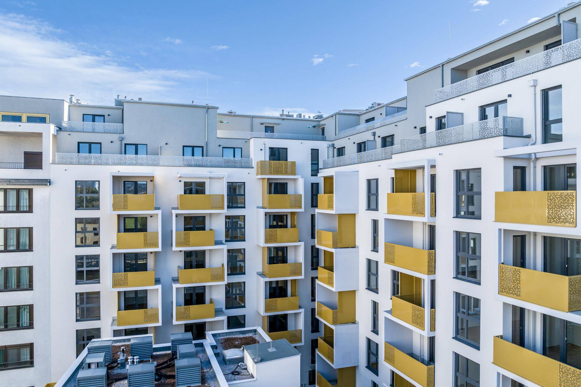 Moderne Wohngebäude mit weißen Fassaden und auffälligen gelben Balkonen unter blauem Himmel.