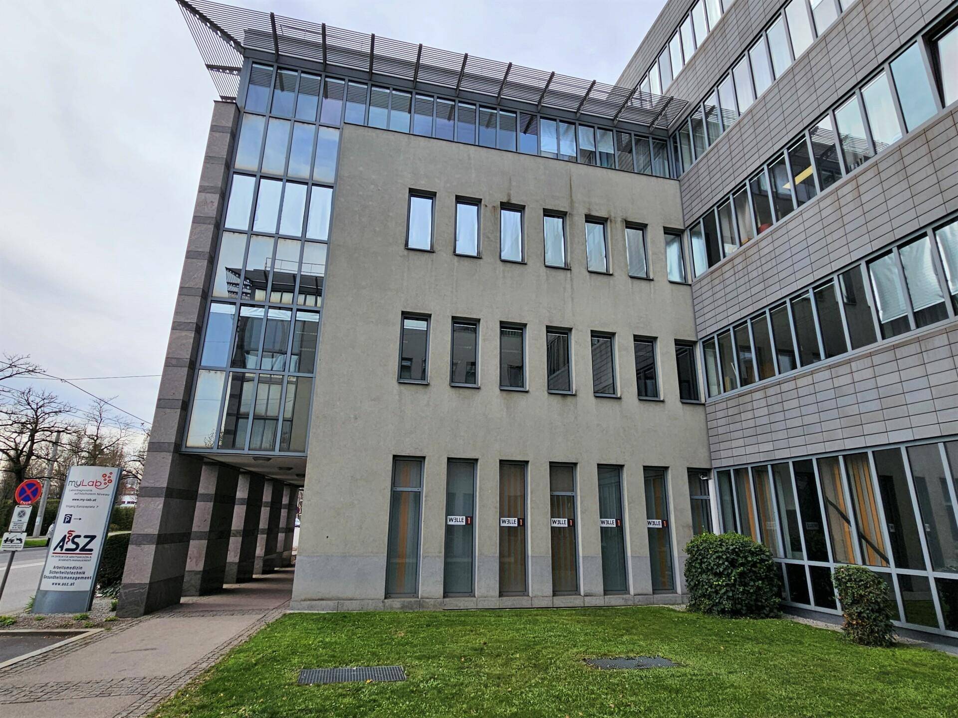 Ansicht eines modernen Bürogebäudes mit großen Glasflächen und einer gepflegten Rasenfläche.