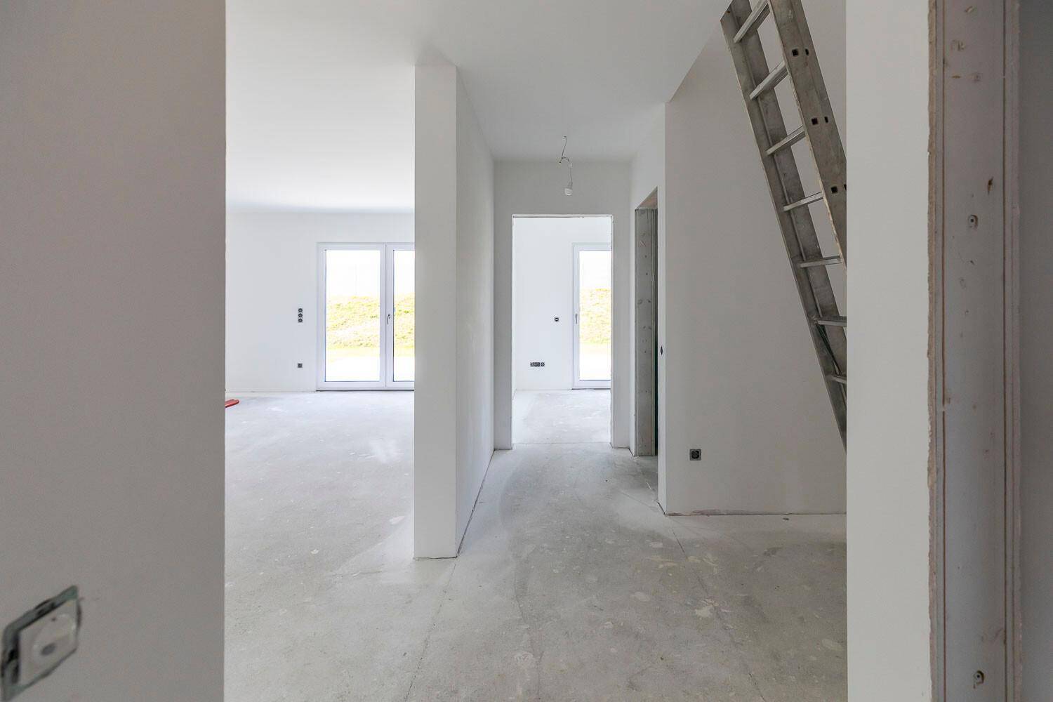 Unfertiger Flur in einem Neubau mit Betonboden, weißen Wänden und einer Leiter.