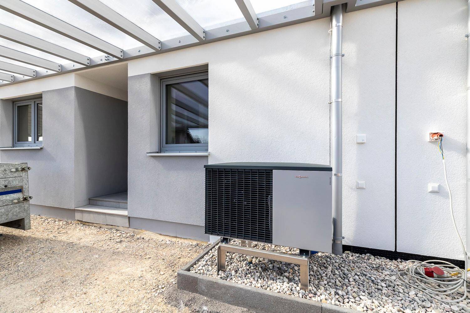 Außenansicht eines Neubaus mit installierter Wärmepumpe und überdachtem Bereich.