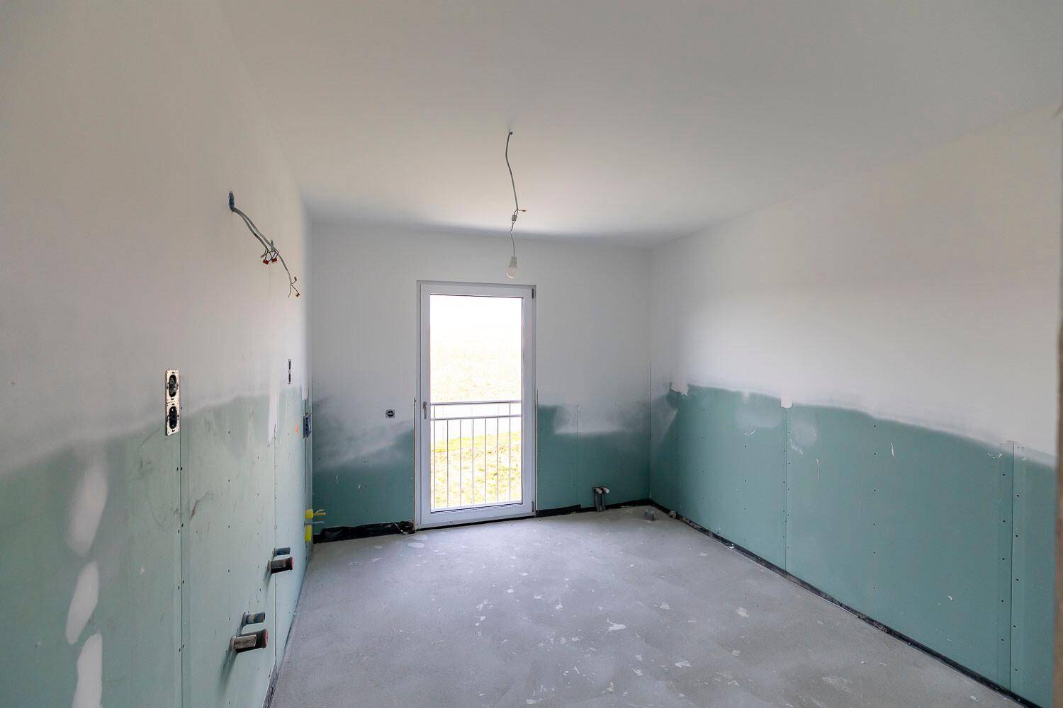 Unfertiges Badezimmer mit grünen Trockenbauwänden, Betonboden und französischem Balkon.