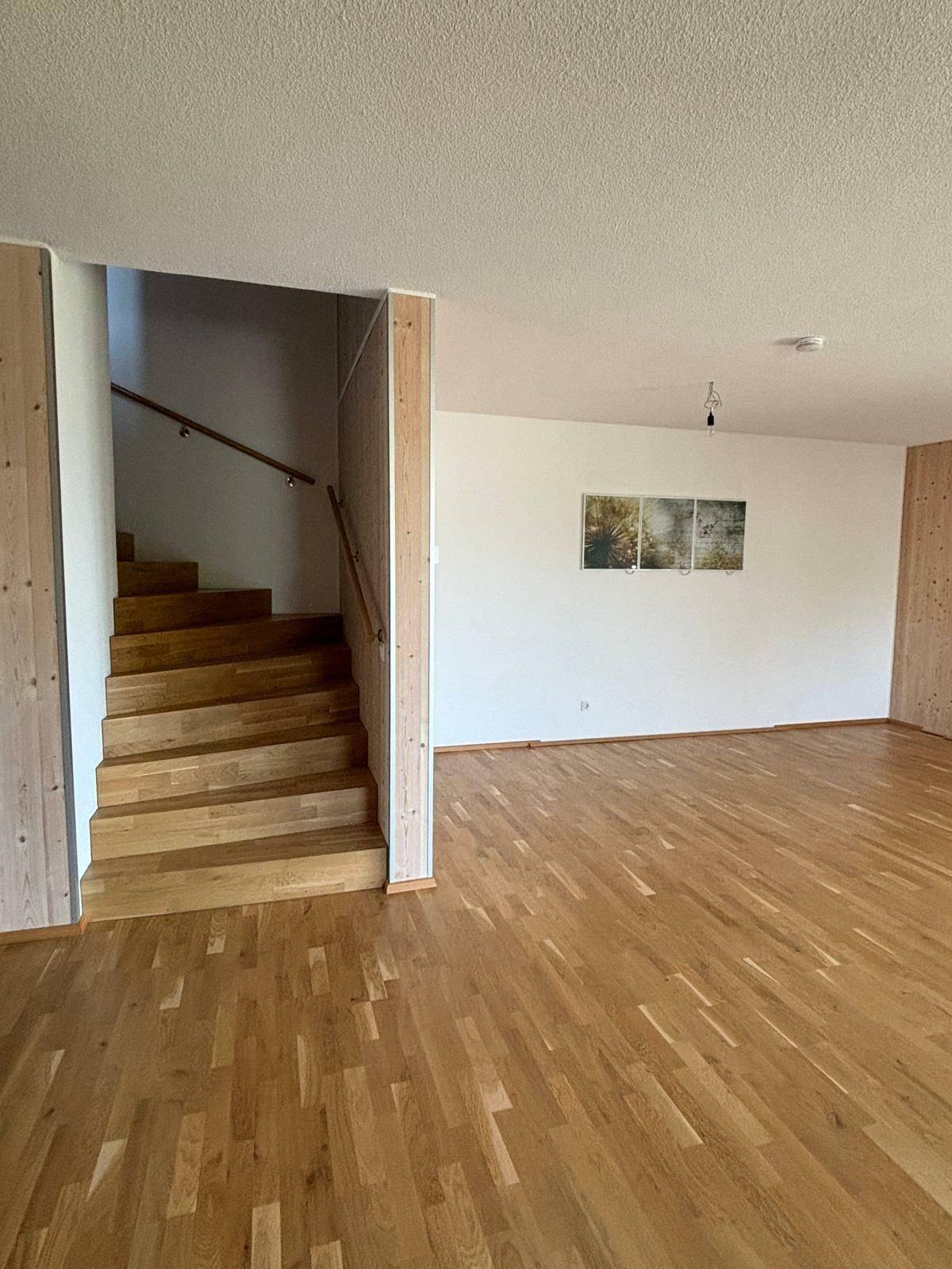 Heller Wohnbereich mit Holztreppe und Parkettboden, der verschiedene Ebenen verbindet.