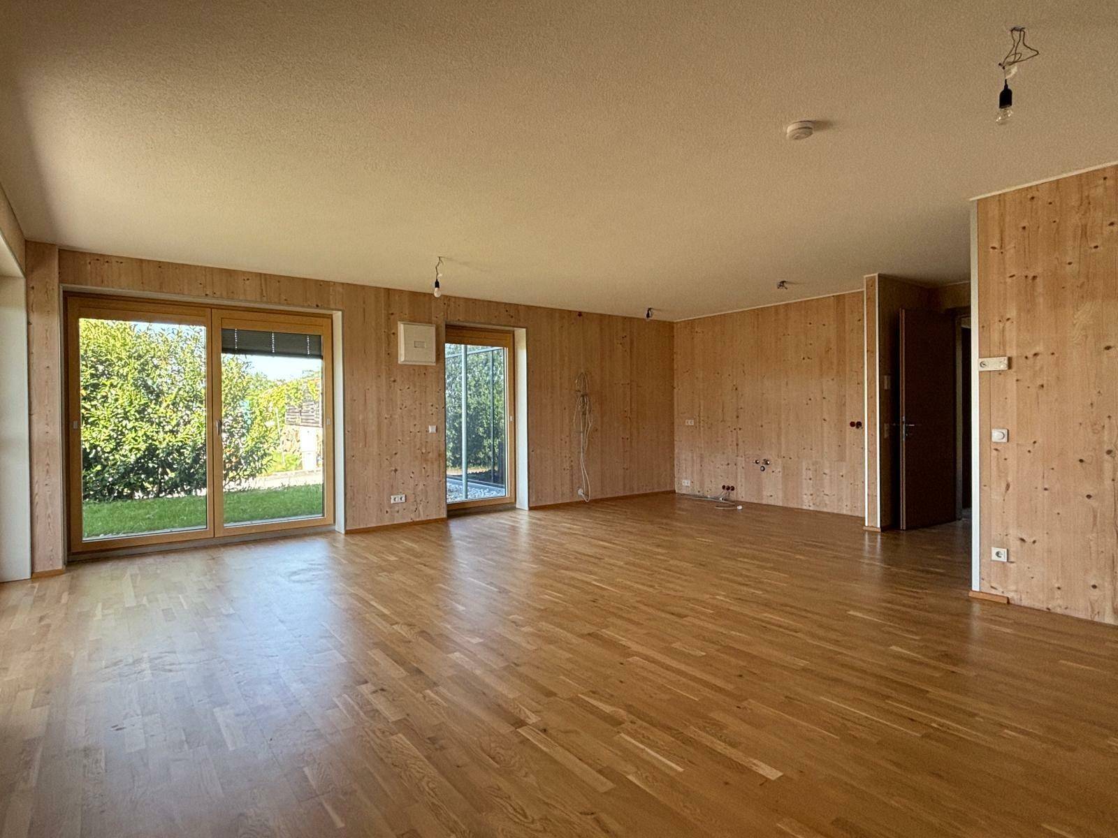 Geräumiges Wohnzimmer mit hellen Holzwänden und Parkettboden, bietet viel Gestaltungspotenzial.