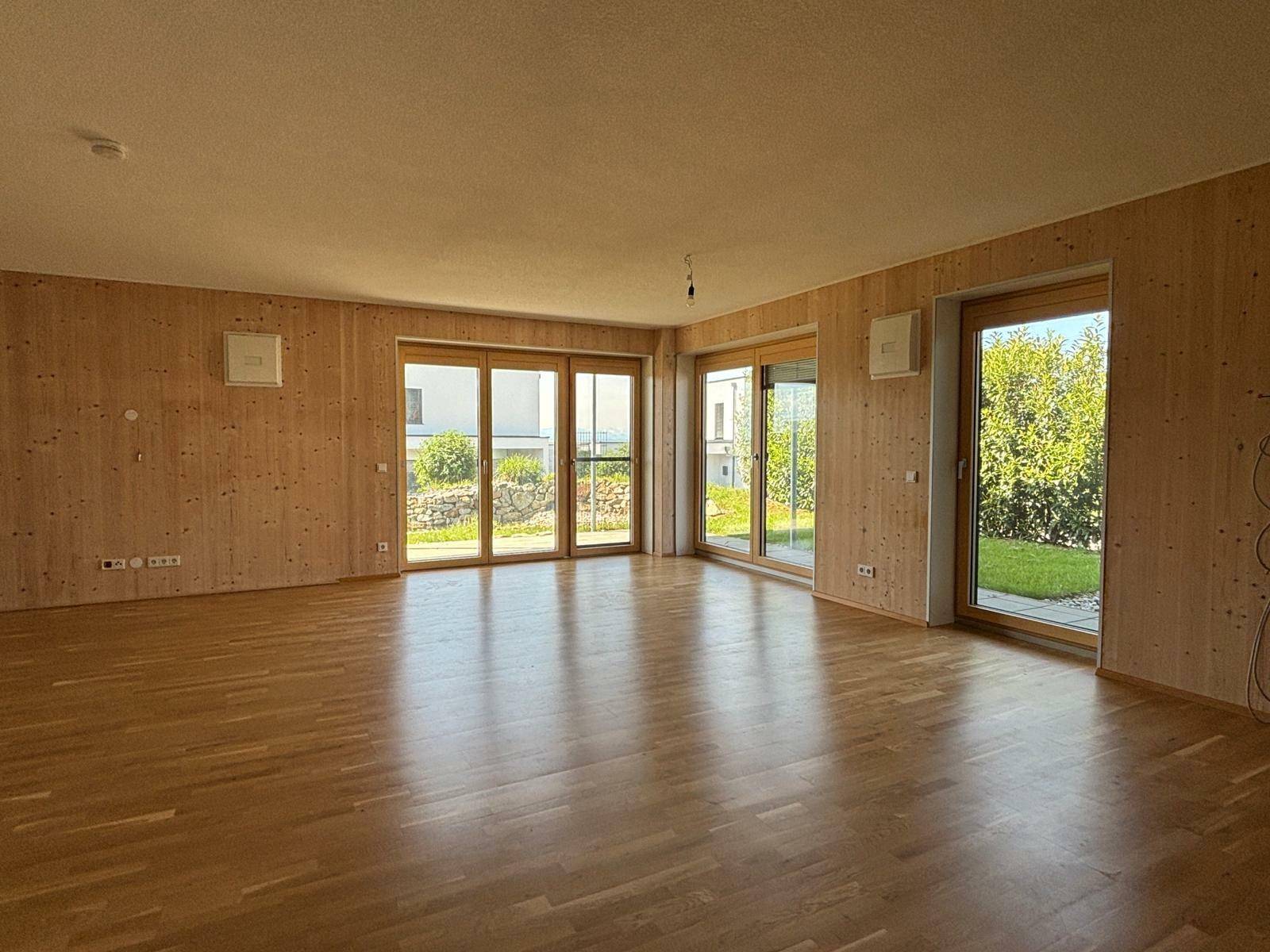 Helles Wohnzimmer mit Holzwänden, Parkettboden und großen Fenstern zum Garten.