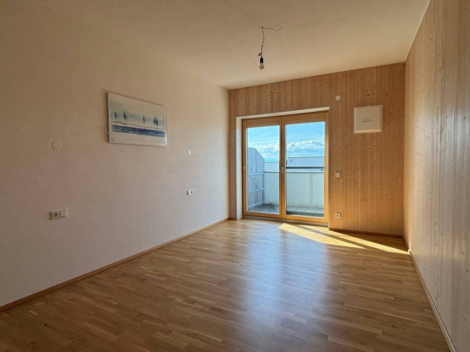 Helles Schlafzimmer mit Holzwänden, Parkettboden und Zugang zu einem privaten Balkon.