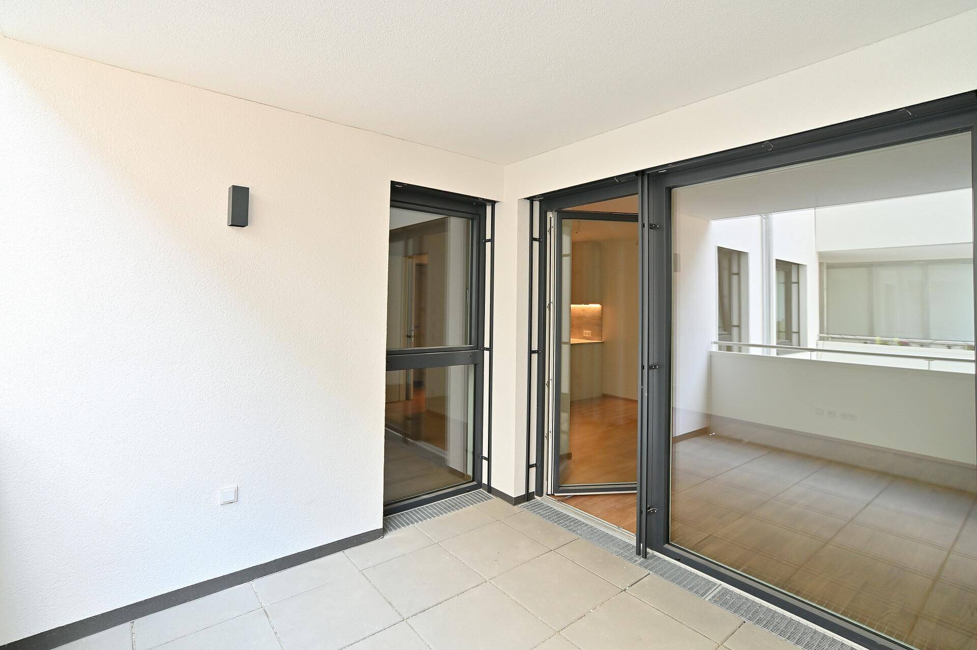 Gefliester Balkon mit schwarzem Geländer und Blick auf den Innenhof des Neubaus.
