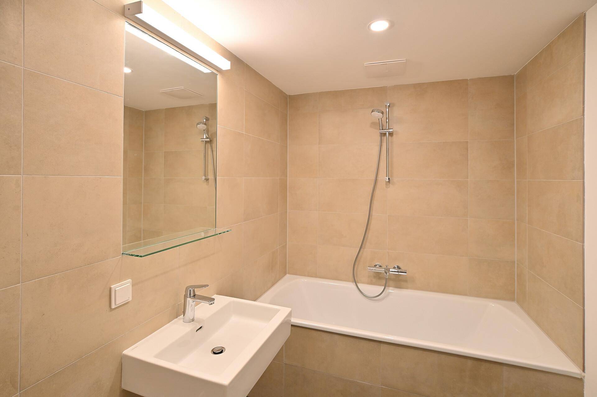 Modernes Badezimmer mit Badewanne, Waschtisch und beigefarbenen Fliesen in einwandfreiem Zustand.