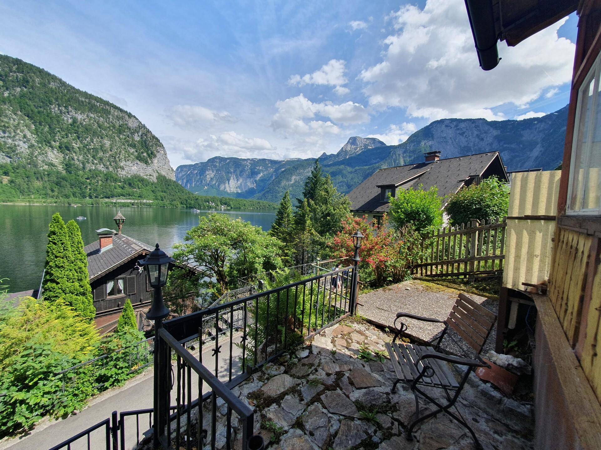 Rustikaler Außensitzbereich mit Steinplatten und einer Bank, mit Blick auf den See und die Berge.