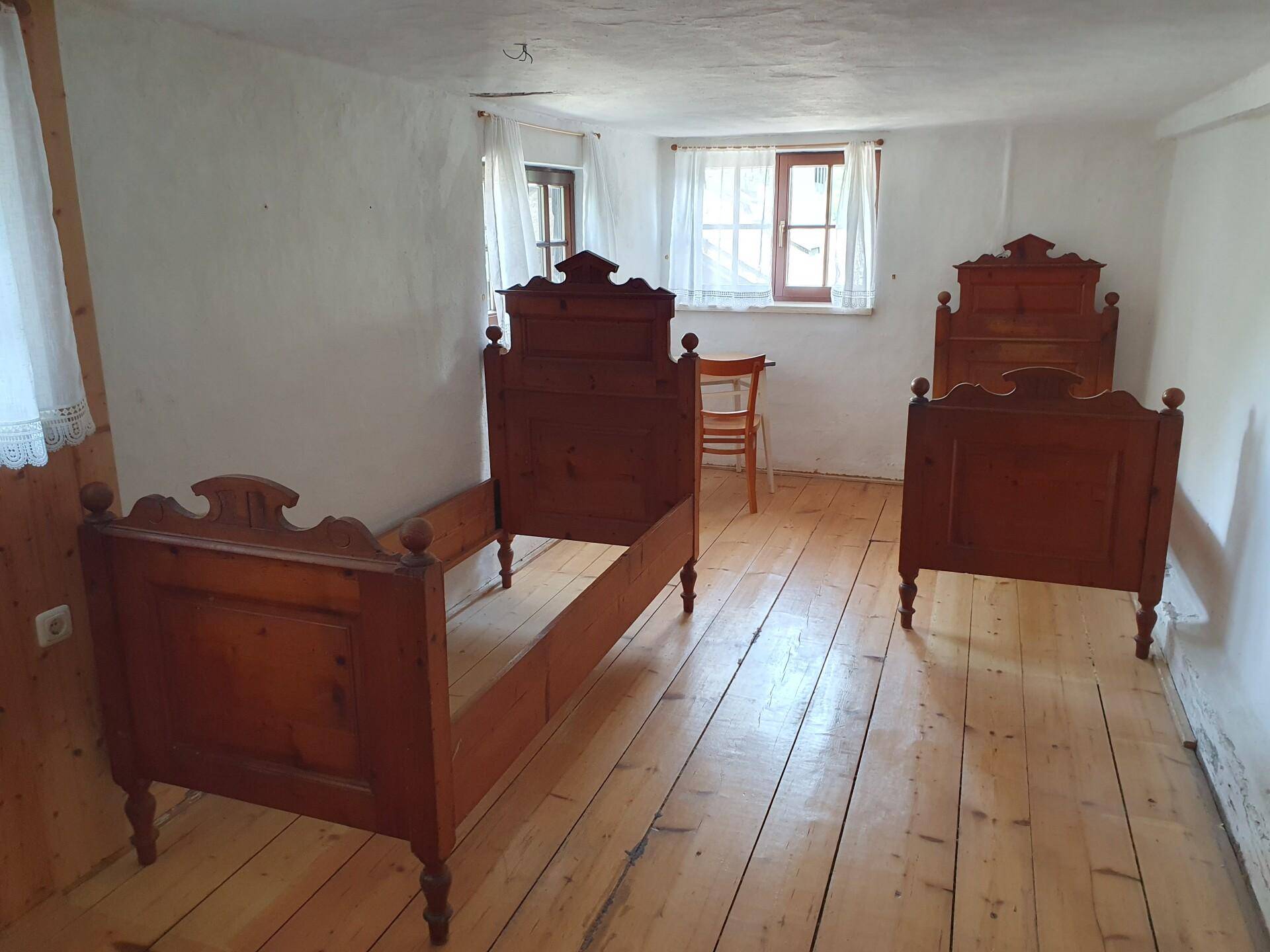 Schlichtes Schlafzimmer mit zwei antiken Holzbetten und einem hellen Holzdielenboden.