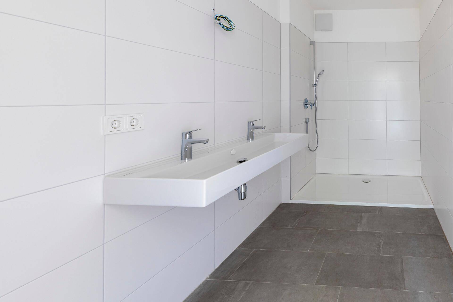 Modernes Badezimmer mit Doppelwaschbecken, ebenerdiger Dusche und weißen Wandfliesen.