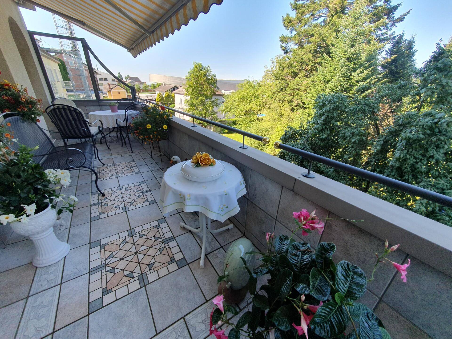 Möblierter Balkon mit gemusterten Fliesen, Markise und Blick ins Grüne.