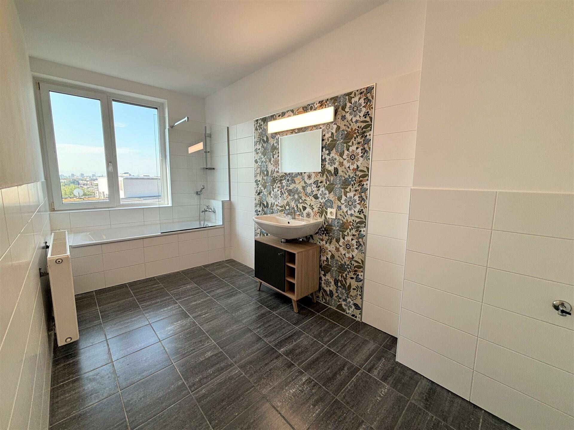 Modernes Badezimmer mit Badewanne, Duschbereich, Fenster und dekorativen Fliesen hinter dem Waschbecken.