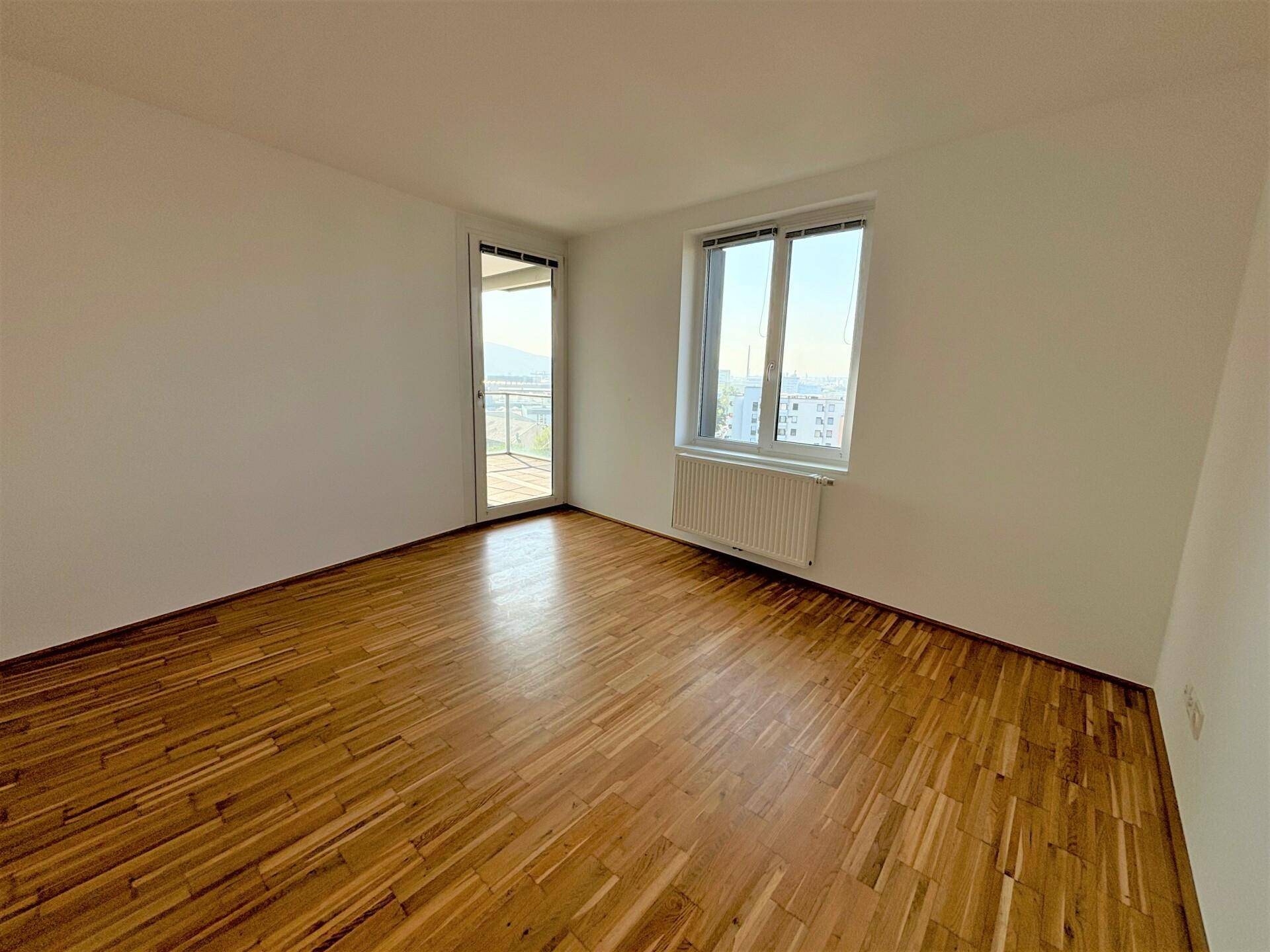 Helles Schlafzimmer mit Holzboden, großem Fenster und Zugang zu einem Balkon.