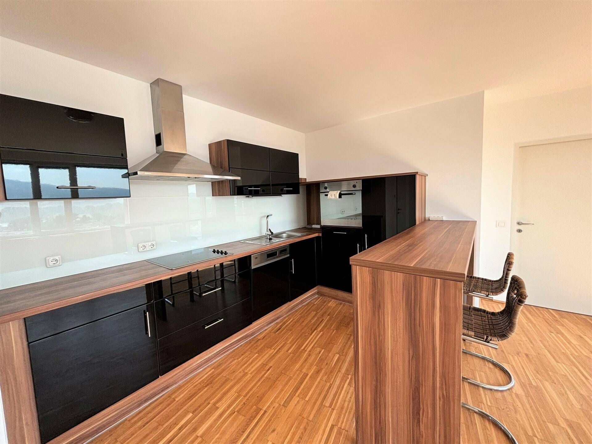 Moderne Küche mit schwarzen Hochglanzfronten, Holzarbeitsplatten und einer Frühstücksbar mit Hockern.