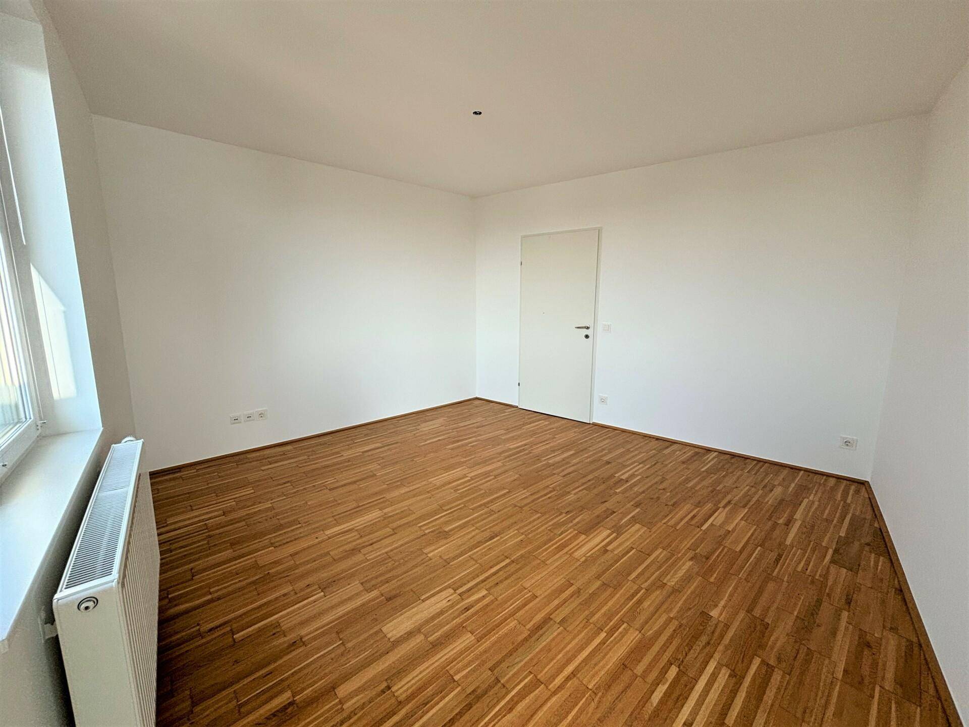 Leeres Zimmer mit Holzboden und einem großen Fenster, bereit zur individuellen Gestaltung.