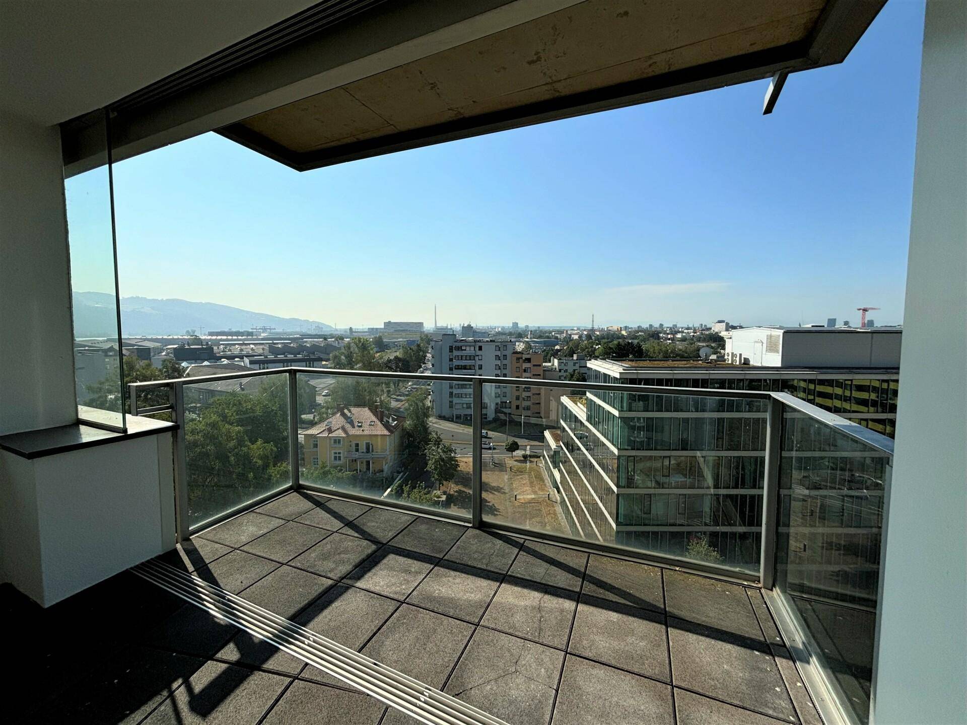 Balkon mit Glasbrüstung und weitem Blick über die Stadt und die umliegenden Berge.