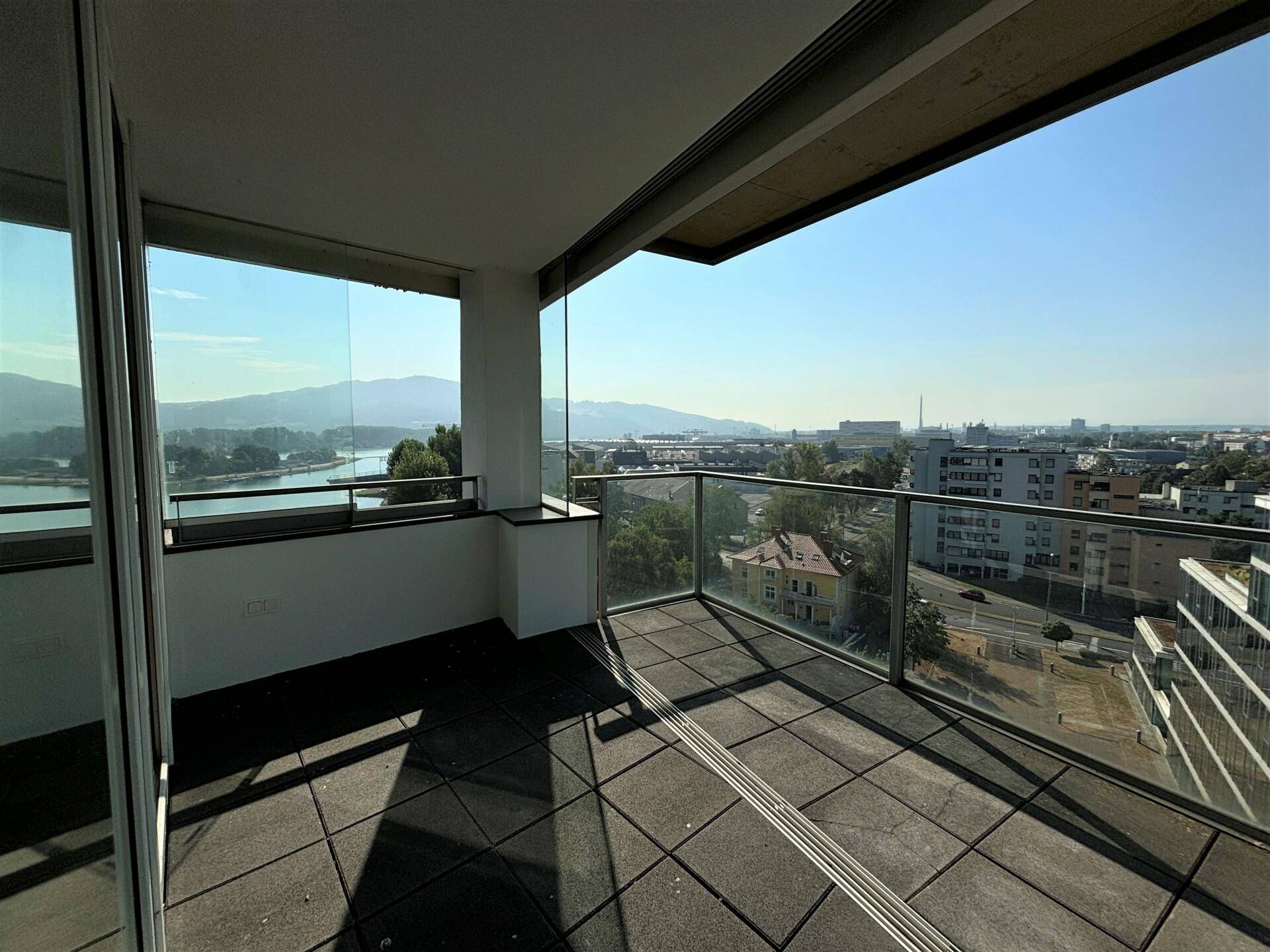 Geräumiger Balkon mit Glasgeländer und Panoramablick auf die Stadt und die Berglandschaft.
