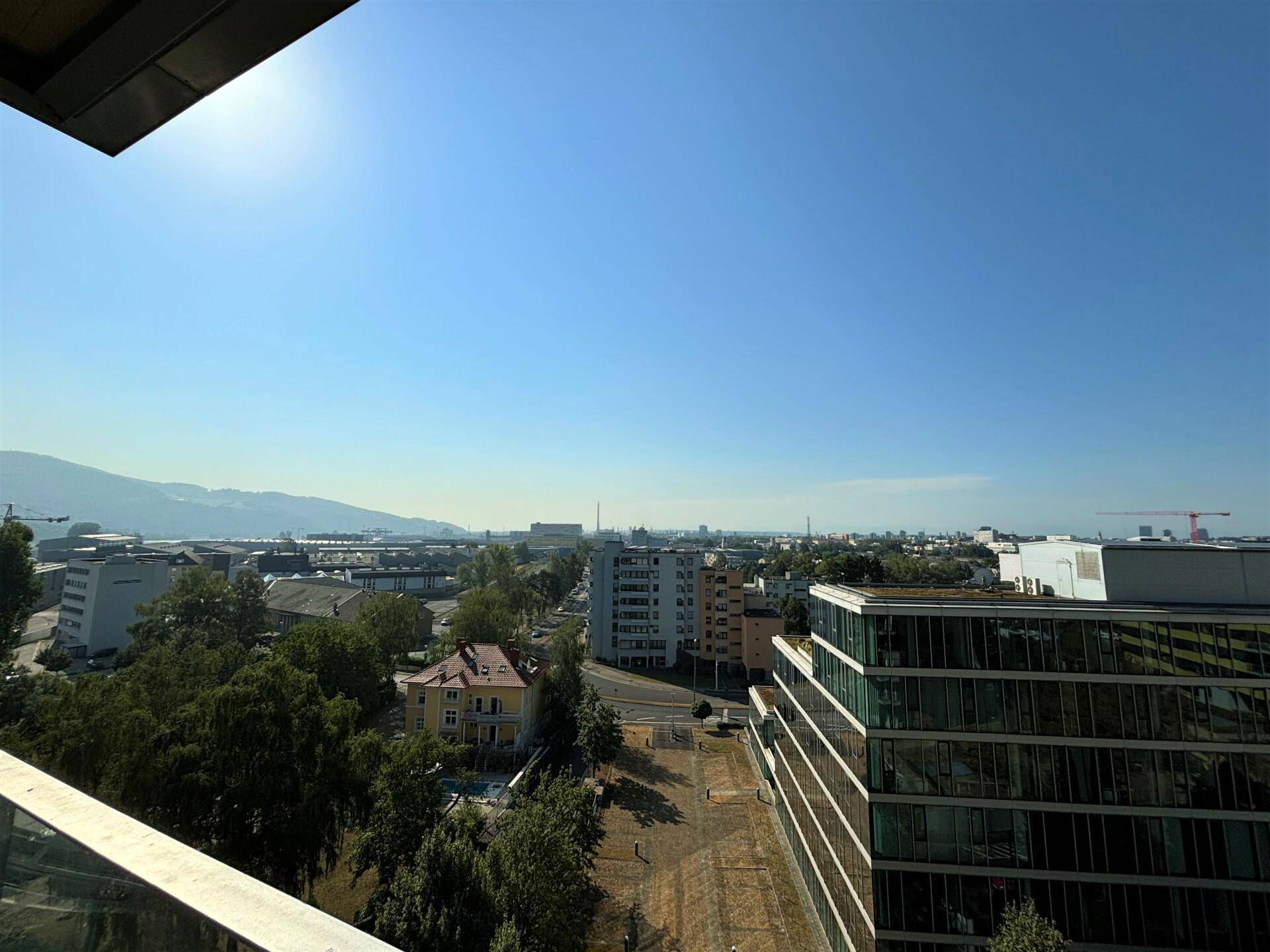 Panoramablick über die Stadt mit modernen Gebäuden und Bergen am Horizont unter blauem Himmel.