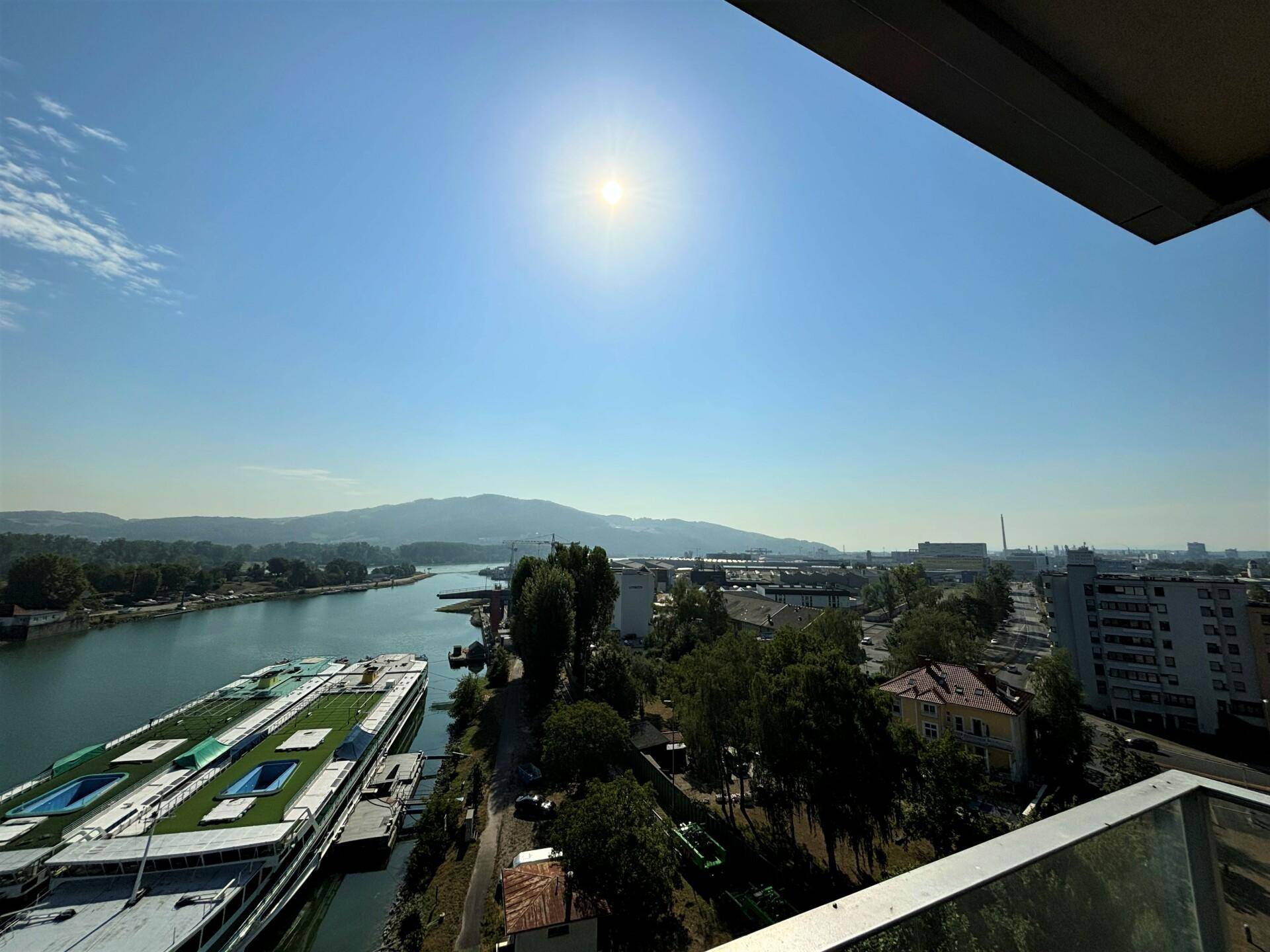 Weitläufiger Ausblick auf den Fluss, die Stadt und die Berge unter strahlendem Sonnenschein.