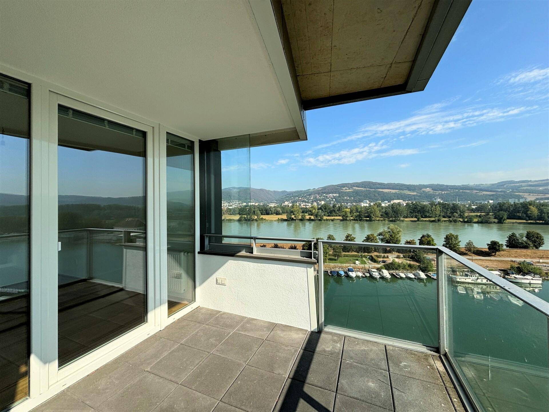 Balkon mit Glasbrüstung und Blick auf den Fluss, den Yachthafen und die bewaldeten Hügel.