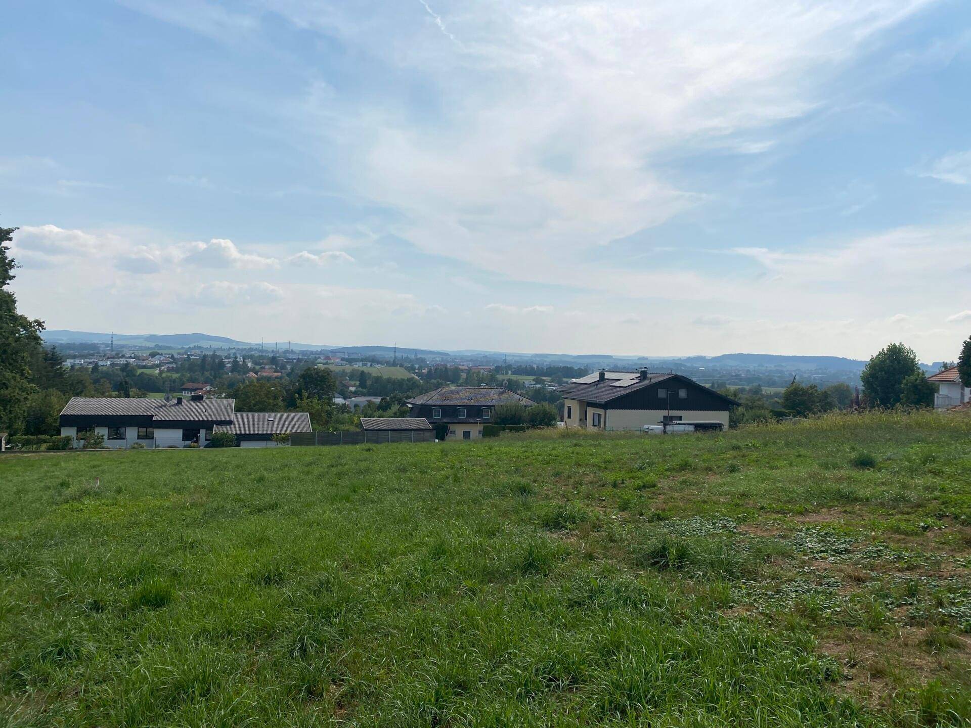 Grüne Wiesenfläche mit Blick auf Wohnhäuser und die hügelige Landschaft unter bewölktem Himmel.