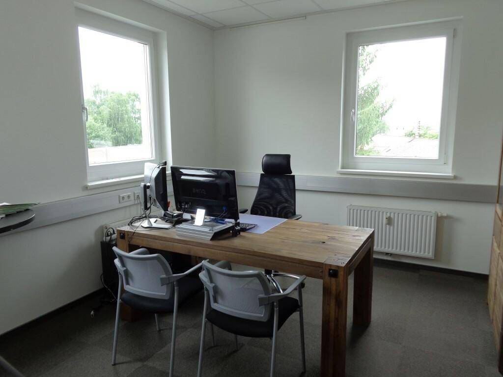 Helles Büro mit einem Holztisch, zwei Stühlen und großen Fenstern mit Blick ins Grüne.