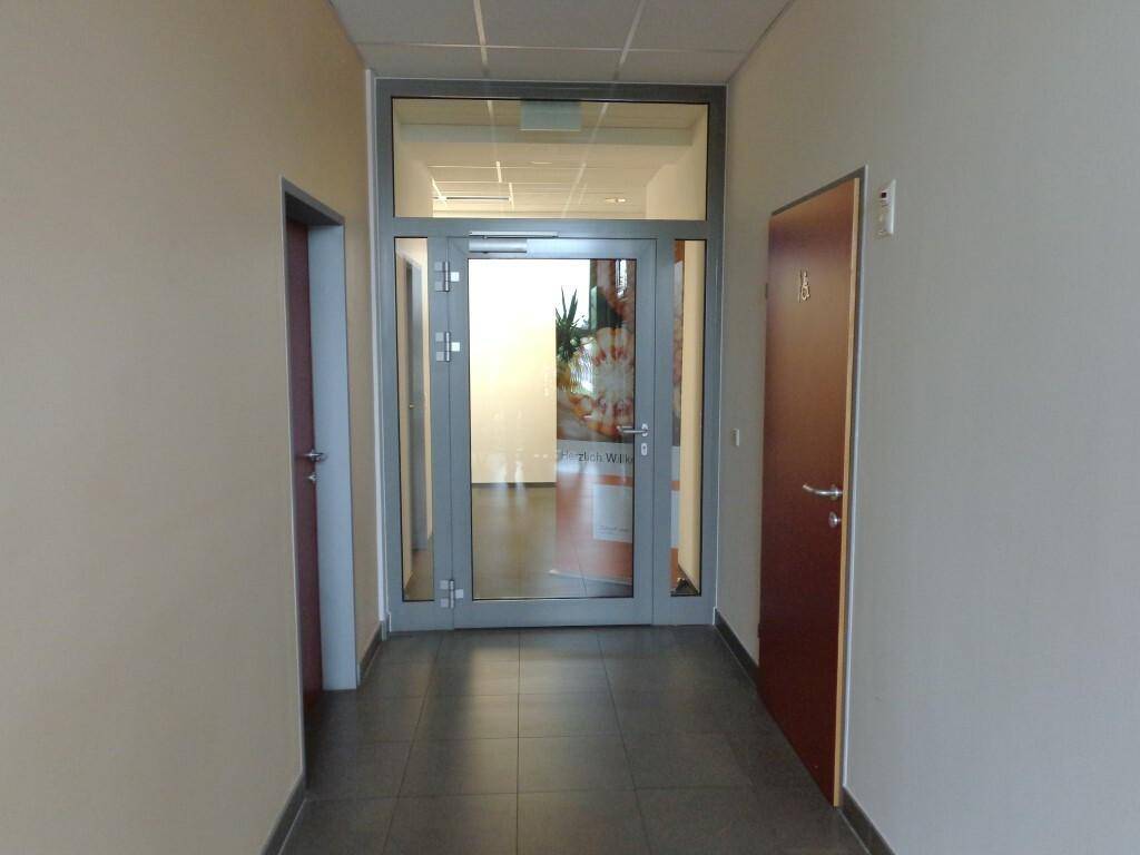 Heller Flur mit Fliesenboden und einer modernen Glastür, die zu einem weiteren Raum führt.