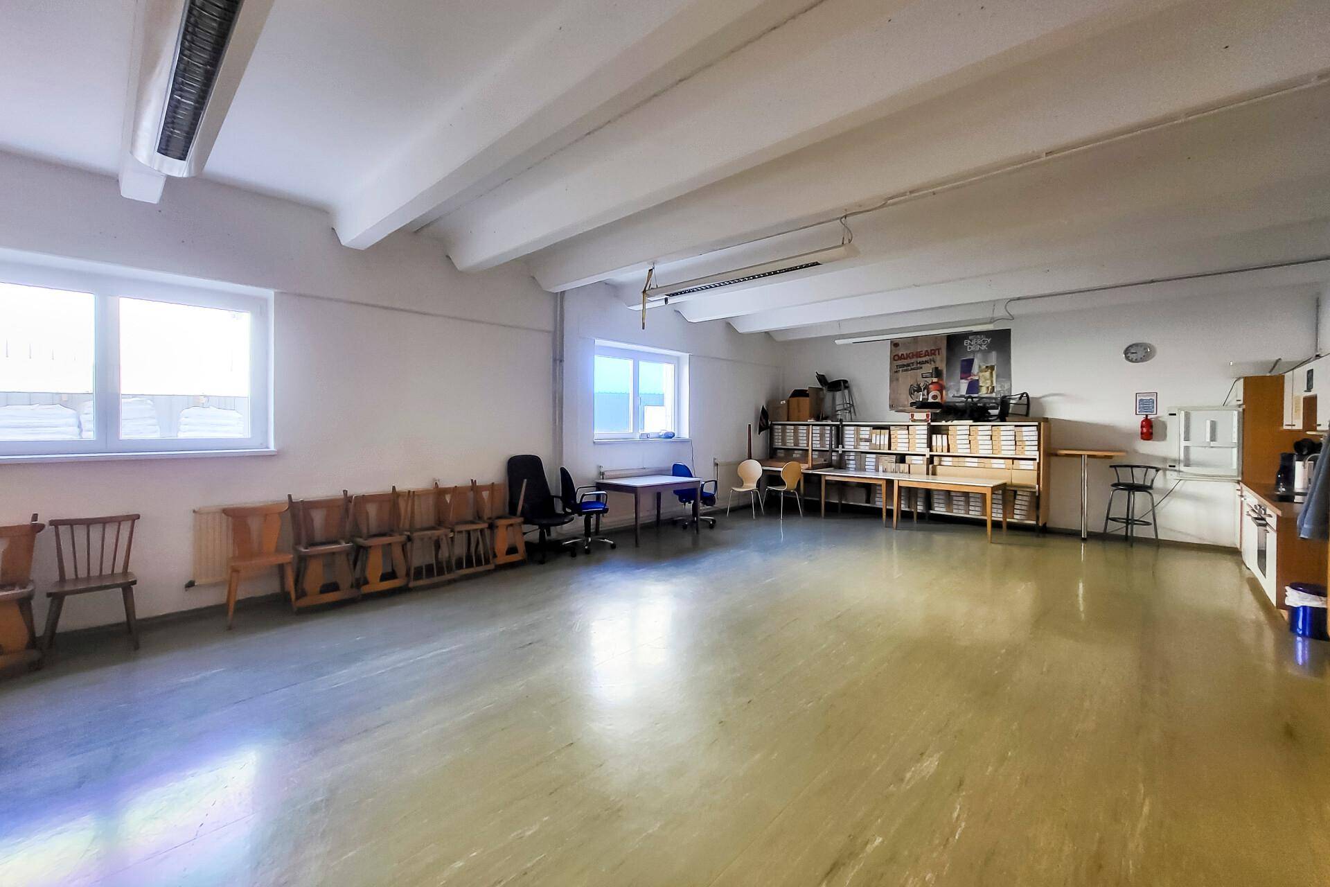 Großer Mehrzweckraum mit hellen Wänden, Fenstern und verschiedenen Möbeln, ideal für Bürozwecke oder Schulungen.