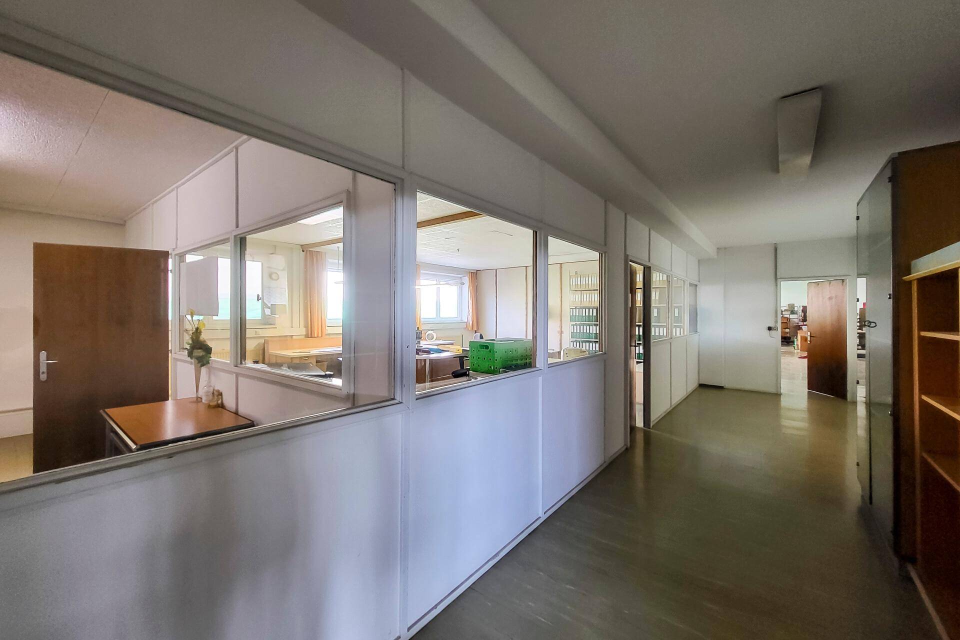 Heller Flur mit Glasabtrennungen zu Büroräumen, bietet viel natürliches Licht und eine offene Atmosphäre.
